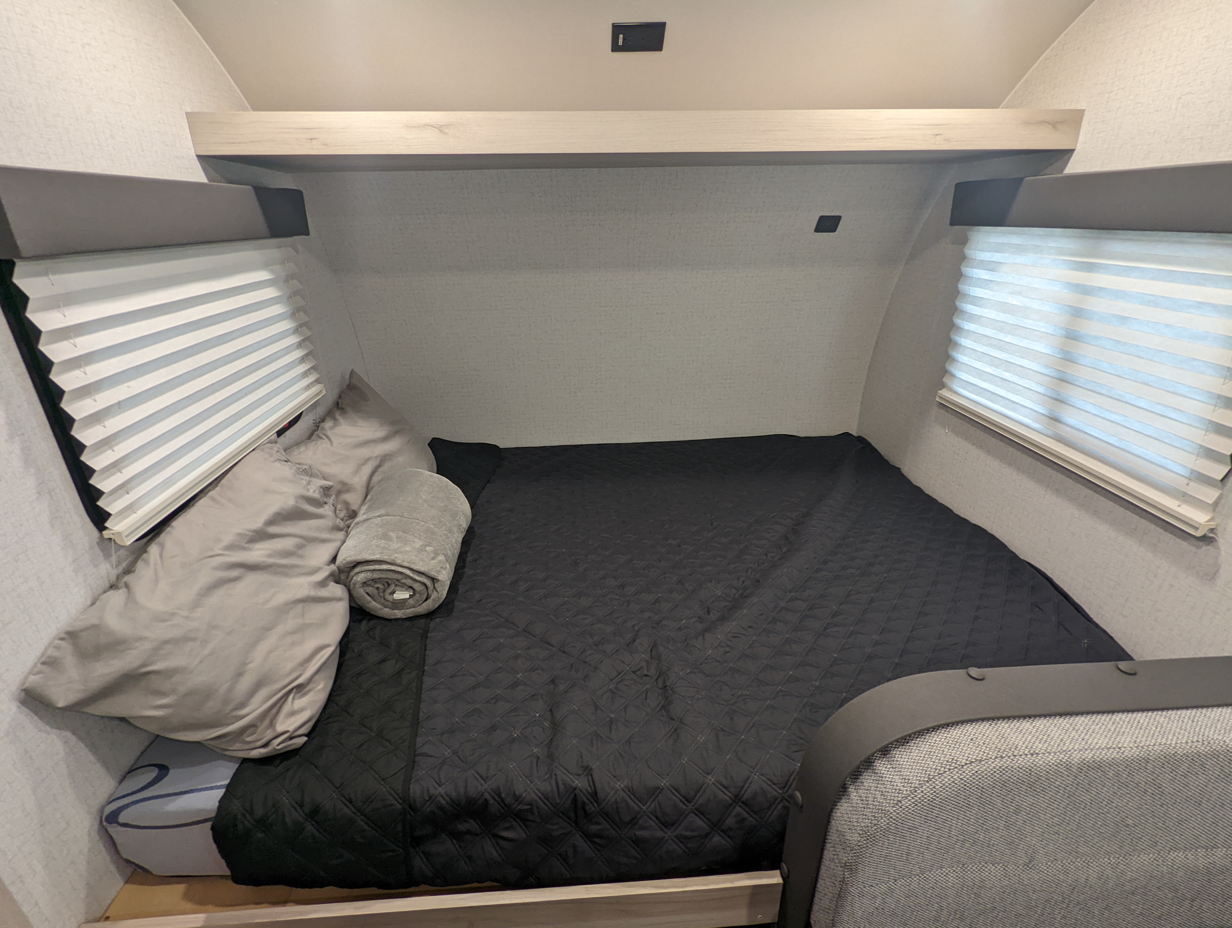 Cozy RV rental bedroom with a black quilted bed, gray pillows, and pleated window blinds.. Winnebago Hike 2022