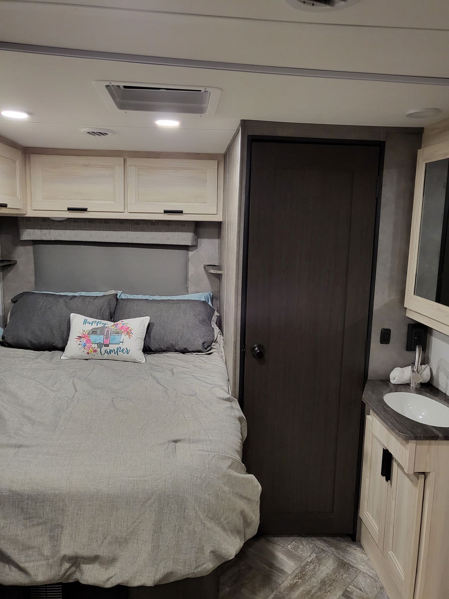 Cozy RV rental interior featuring a bed with overhead cabinets, a compact bathroom vanity with a sink, and a dark door.. Forest River Sunseeker LE 2022