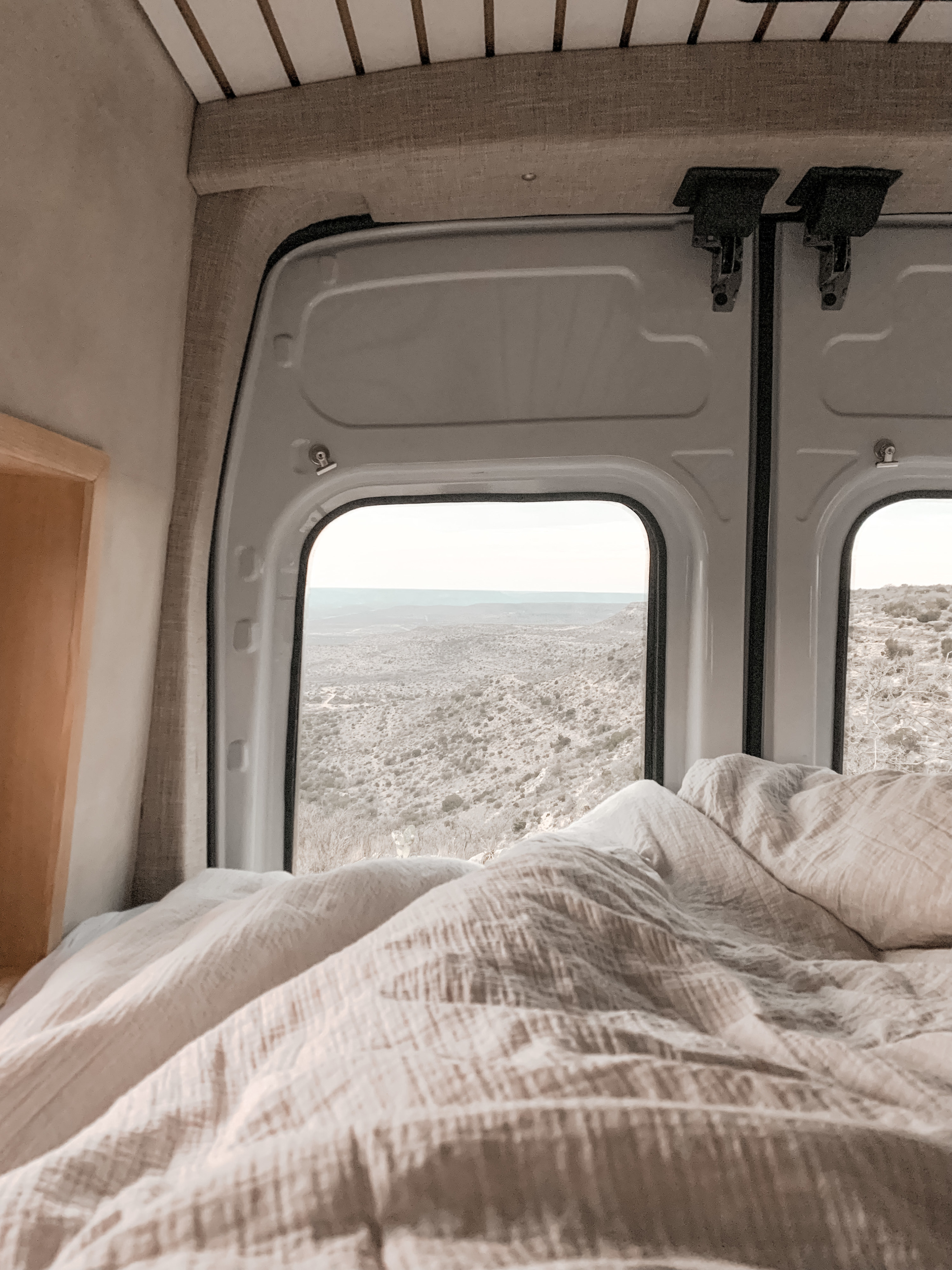 Cozy RV rental bedroom with a stunning desert landscape view from the back windows, perfect for scenic travel.. Ford Transit 2021