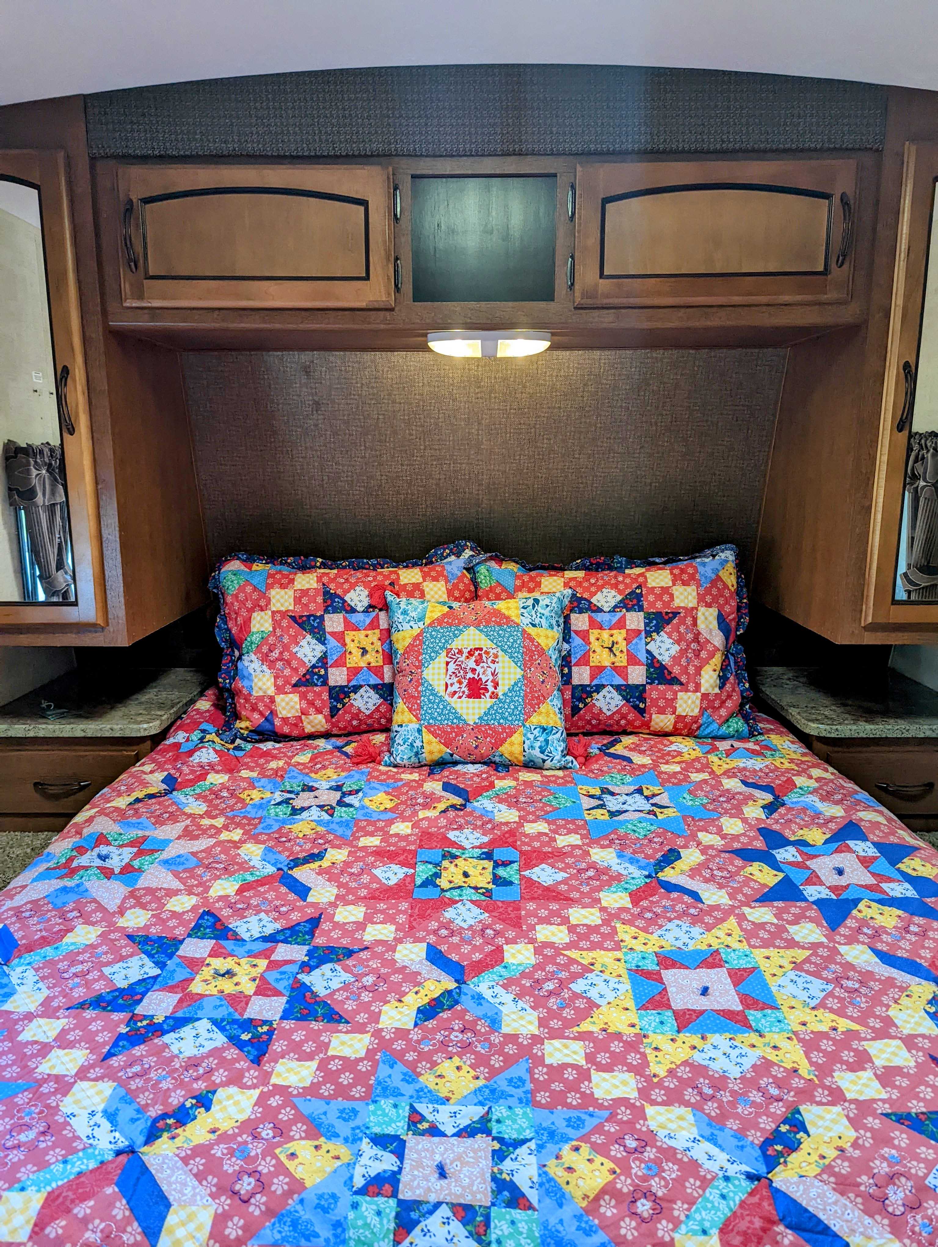 Vibrant quilted bed & pillows in an RV rental, with overhead wood cabinets & lighting.. Keystone RV Springdale 2013