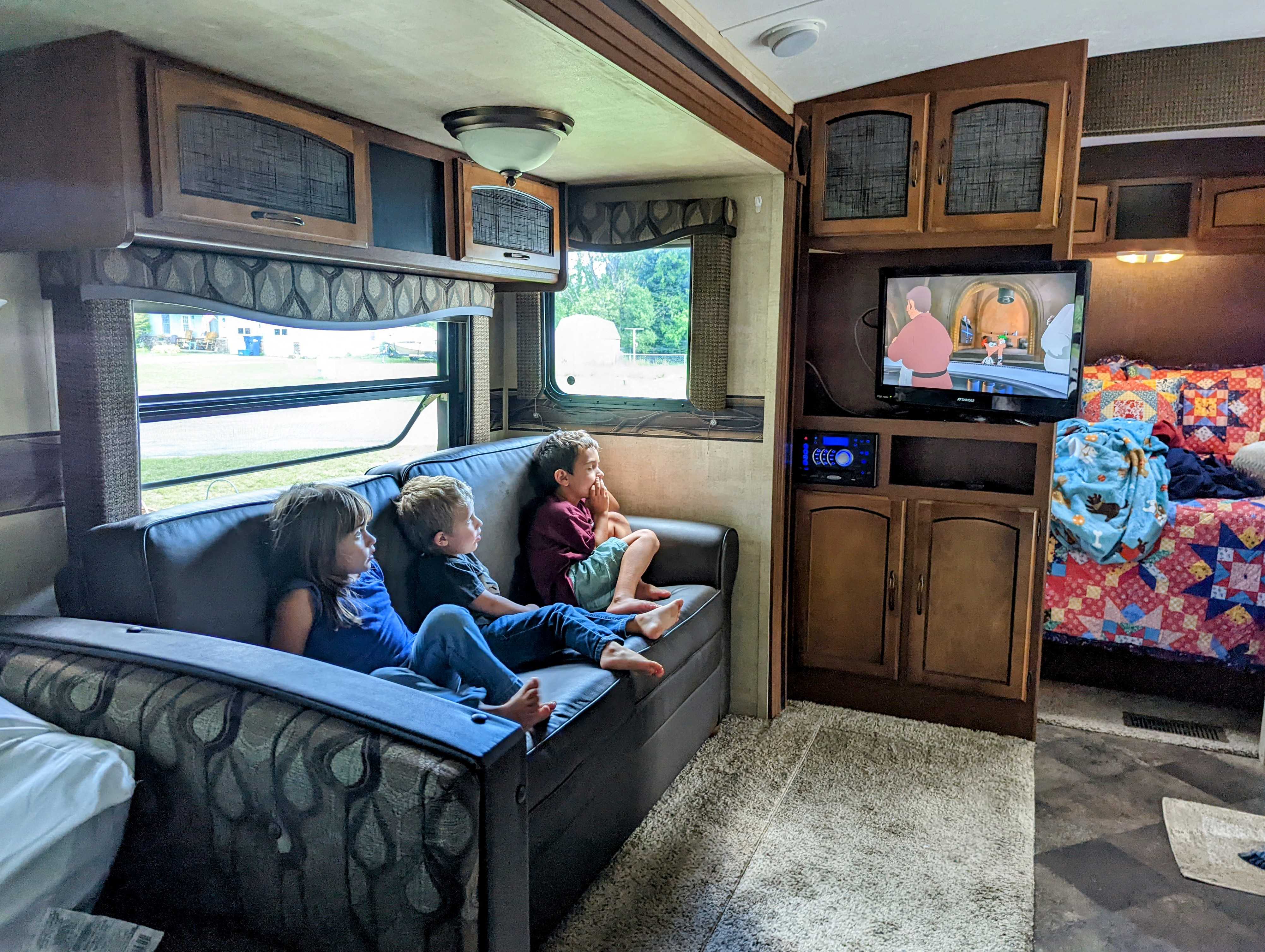 Three kids relax on a sofa watching cartoons on TV inside a cozy RV rental. Ideal for family trips!. Keystone RV Springdale 2013