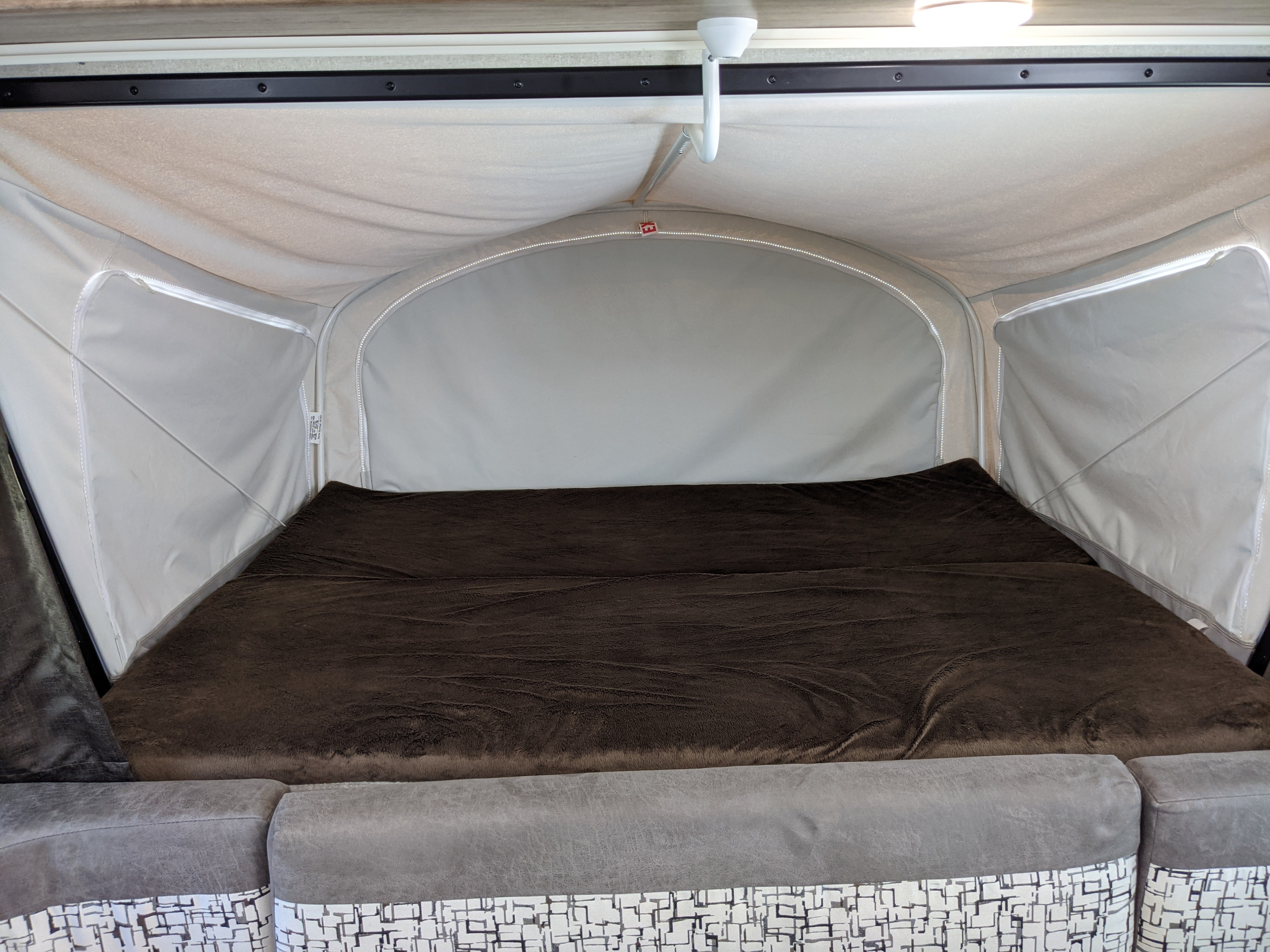 Inside a comfortable pop-up camper: a cozy bed with brown blanket and upholstered seating, great for an RV rental.. Jayco Jay Feather 2019
