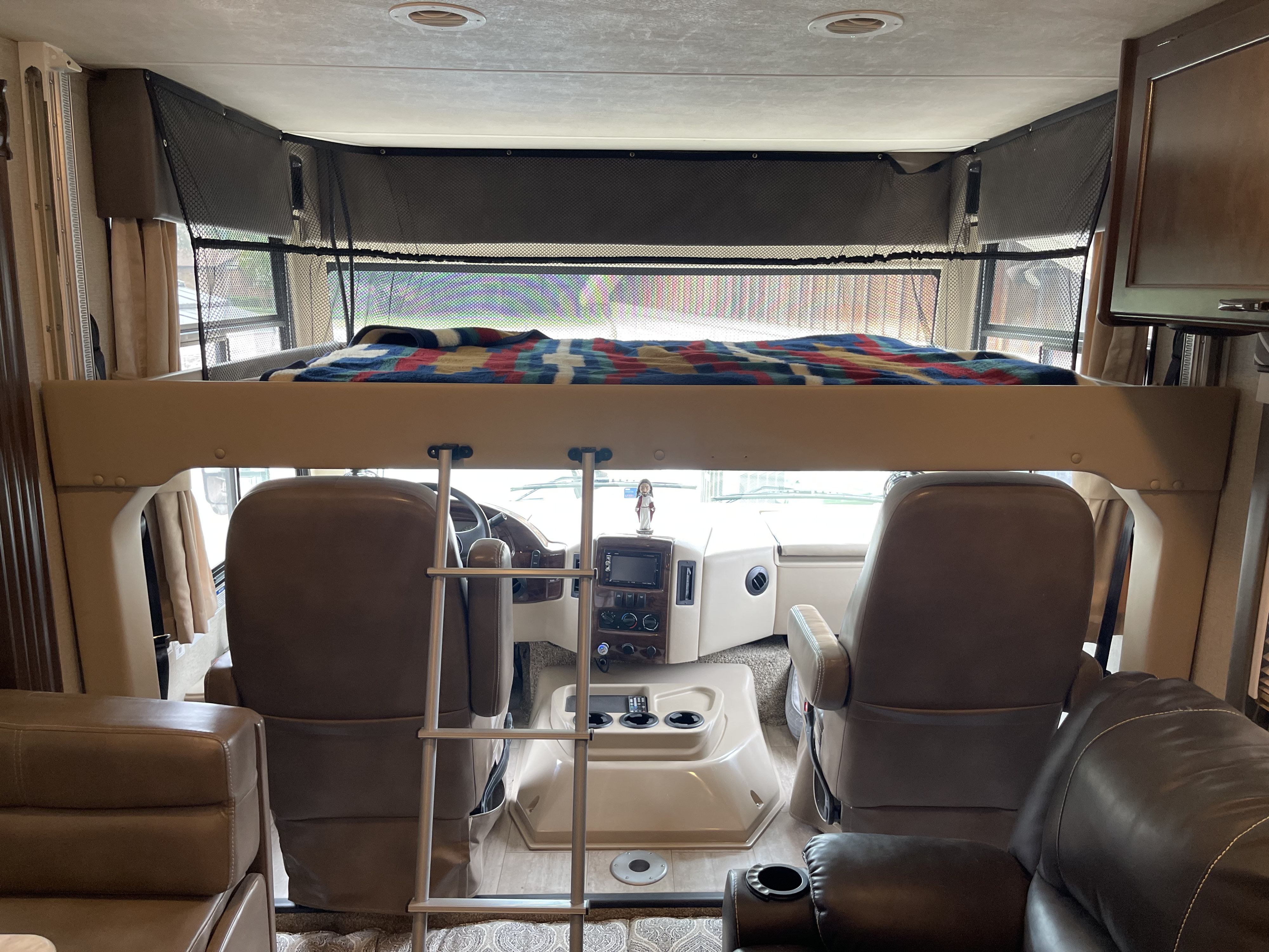 Interior view of an RV rental, highlighting the cab-over bunk bed with safety net, ladder, and front cockpit with seating.. Thor Freedom Traveler 2020