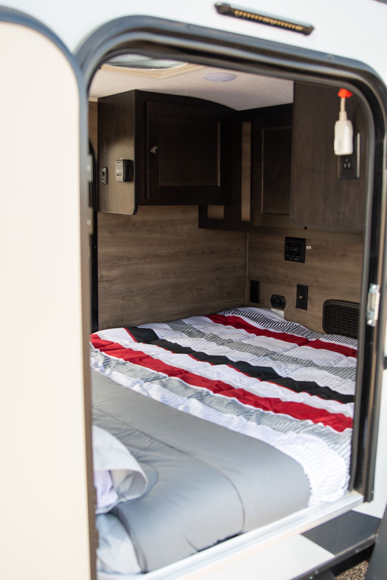 Step inside this RV rental! A compact camper bedroom features a cozy striped bed, dark wood cabinets, and controls.. Braxton Creek Free Solo 2022