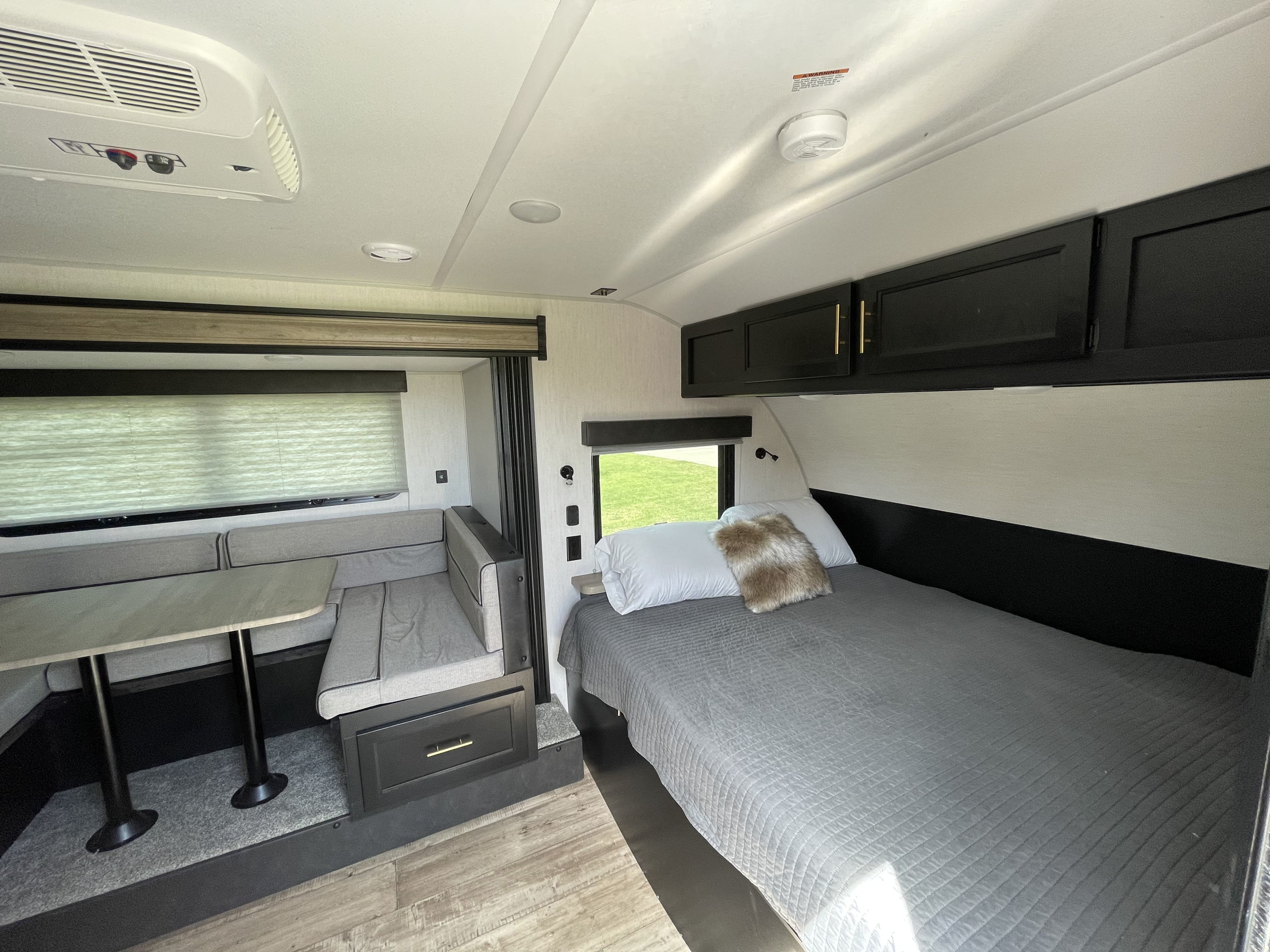 RV rental interior: cozy bed, dinette with table, and overhead storage cabinets. Modern and ready for adventure.. Forest River Cherokee Wolf Pup Black Label 2022