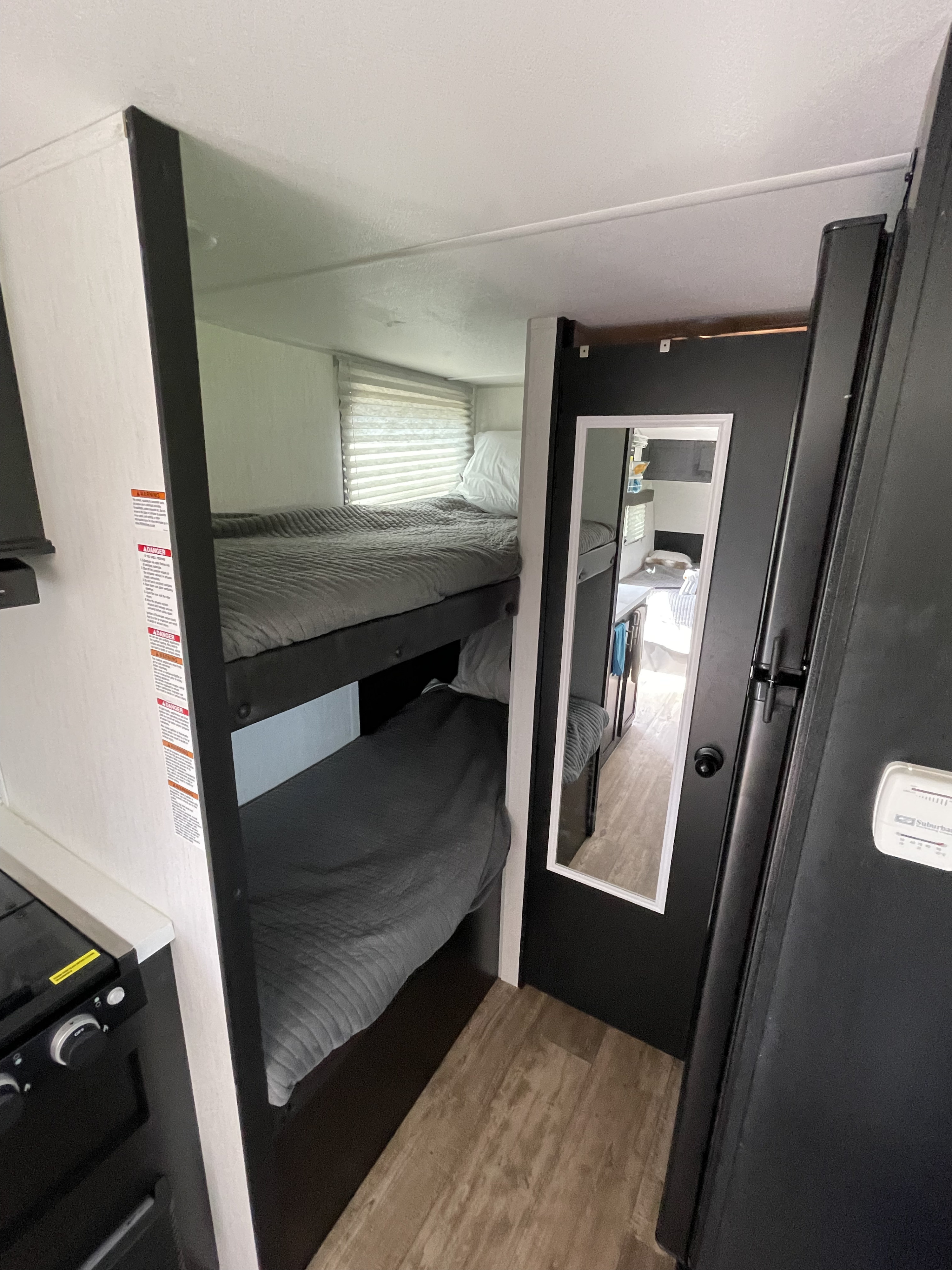 This RV rental features a compact interior with cozy bunk beds and a mirror reflecting the kitchen area, ideal for family adventures.. Forest River Cherokee Wolf Pup Black Label 2022