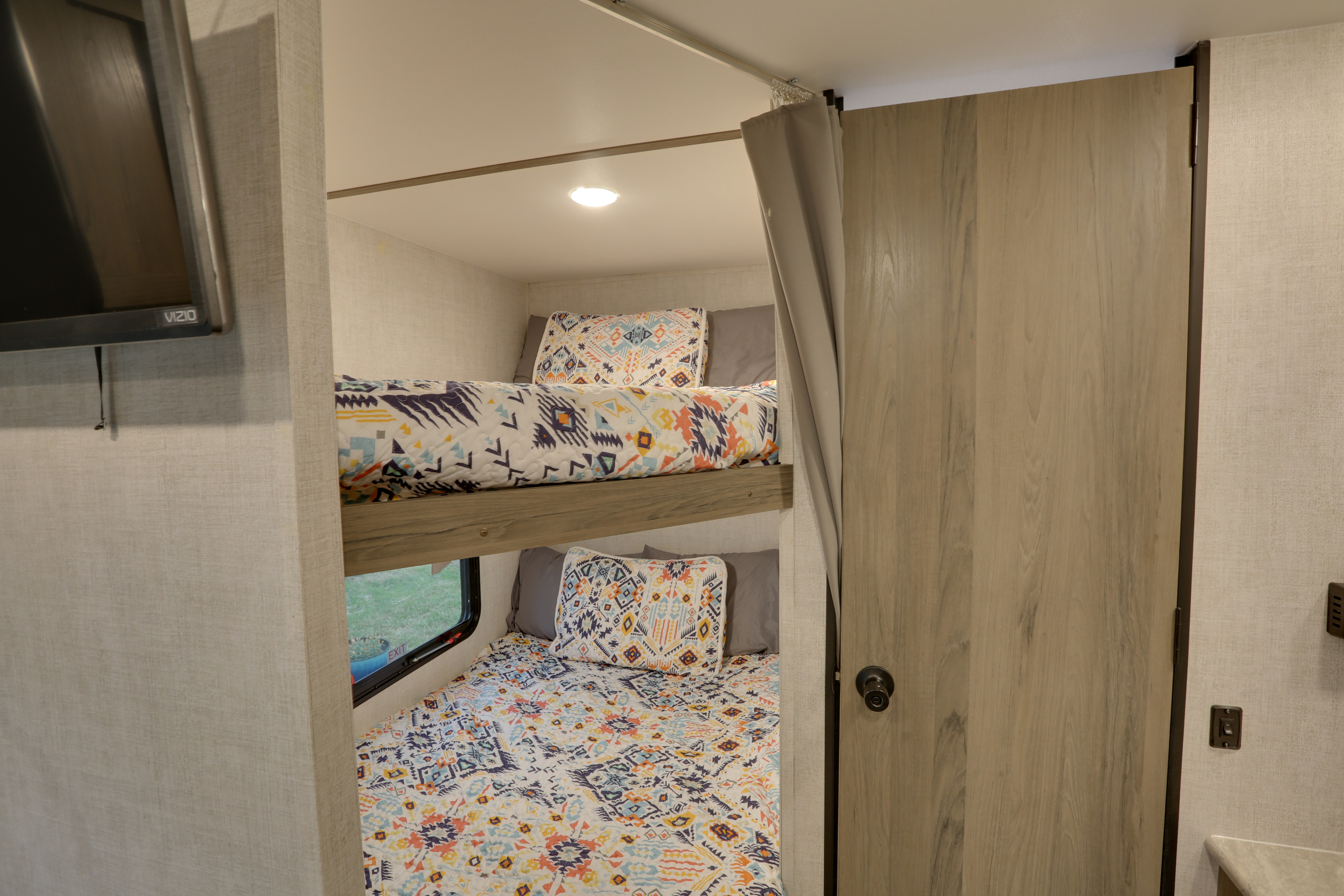Cozy RV rental bunk beds with patterned bedding and window view, adjacent to an interior door.. Gulf Stream Kingsport 2022