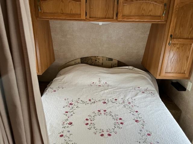 Inside an RV rental: a compact bedroom featuring a bed with a floral quilt and oak wood overhead cabinets.. Keystone RV Summerland 2011