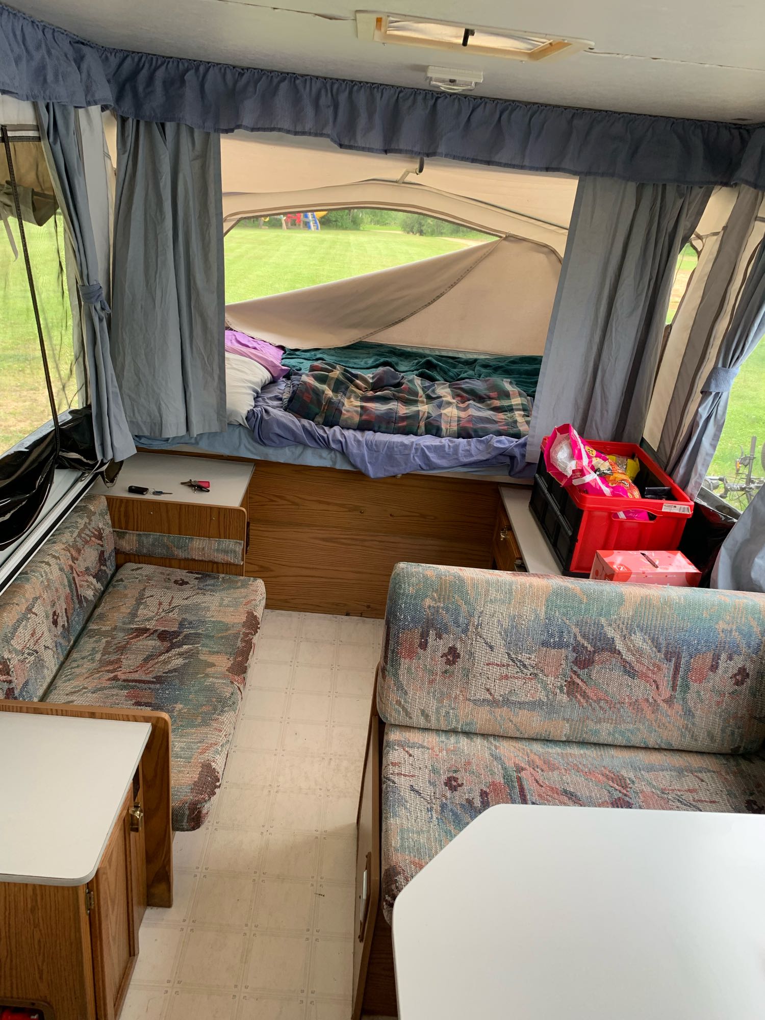 Cozy RV rental interior with a comfortable bed, patterned dinette, and bright outdoor view from a pop-up camper.. Starcraft Starflyer 1996