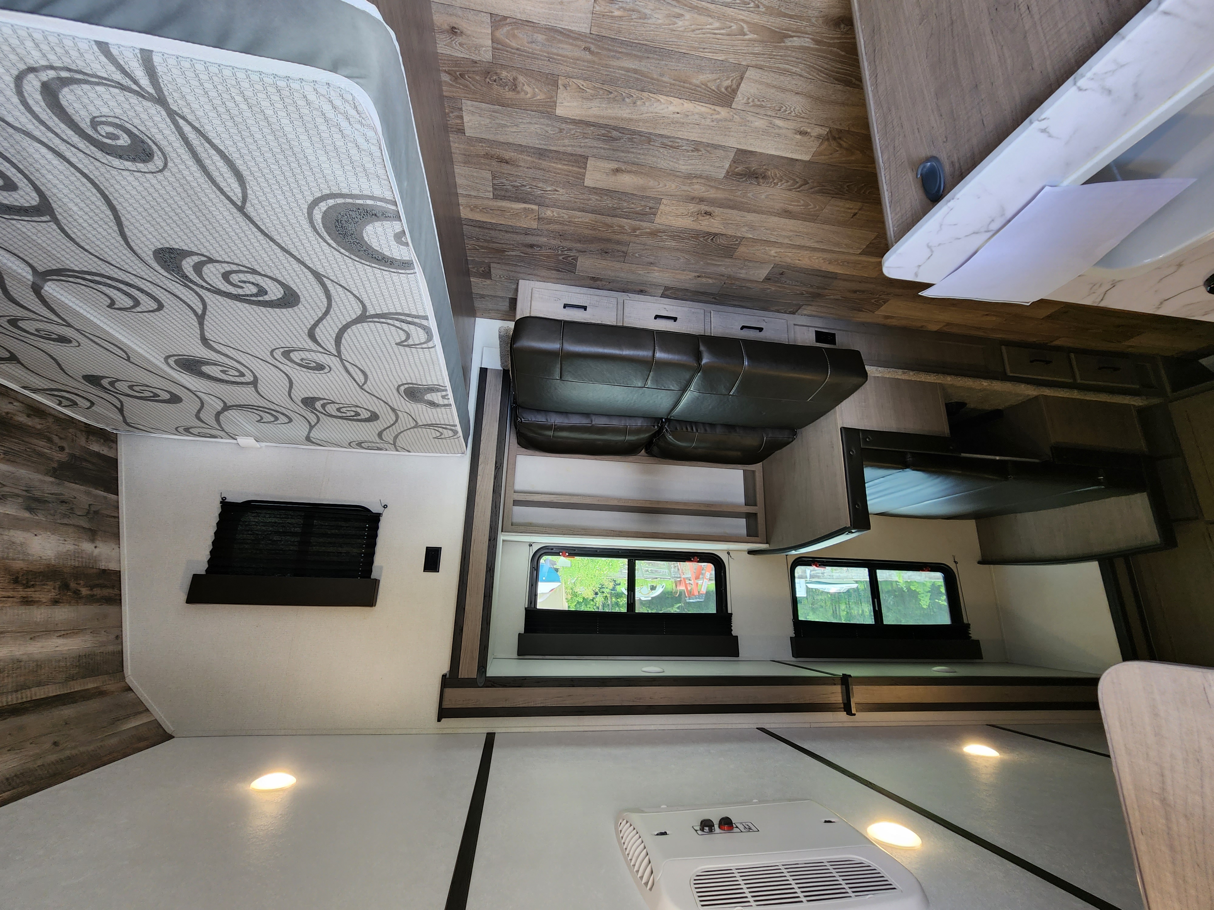 High-angle view of a clean RV rental interior: featuring a comfortable bed, dinette, wood-look flooring, and kitchenette.. Keystone RV Hideout 2022