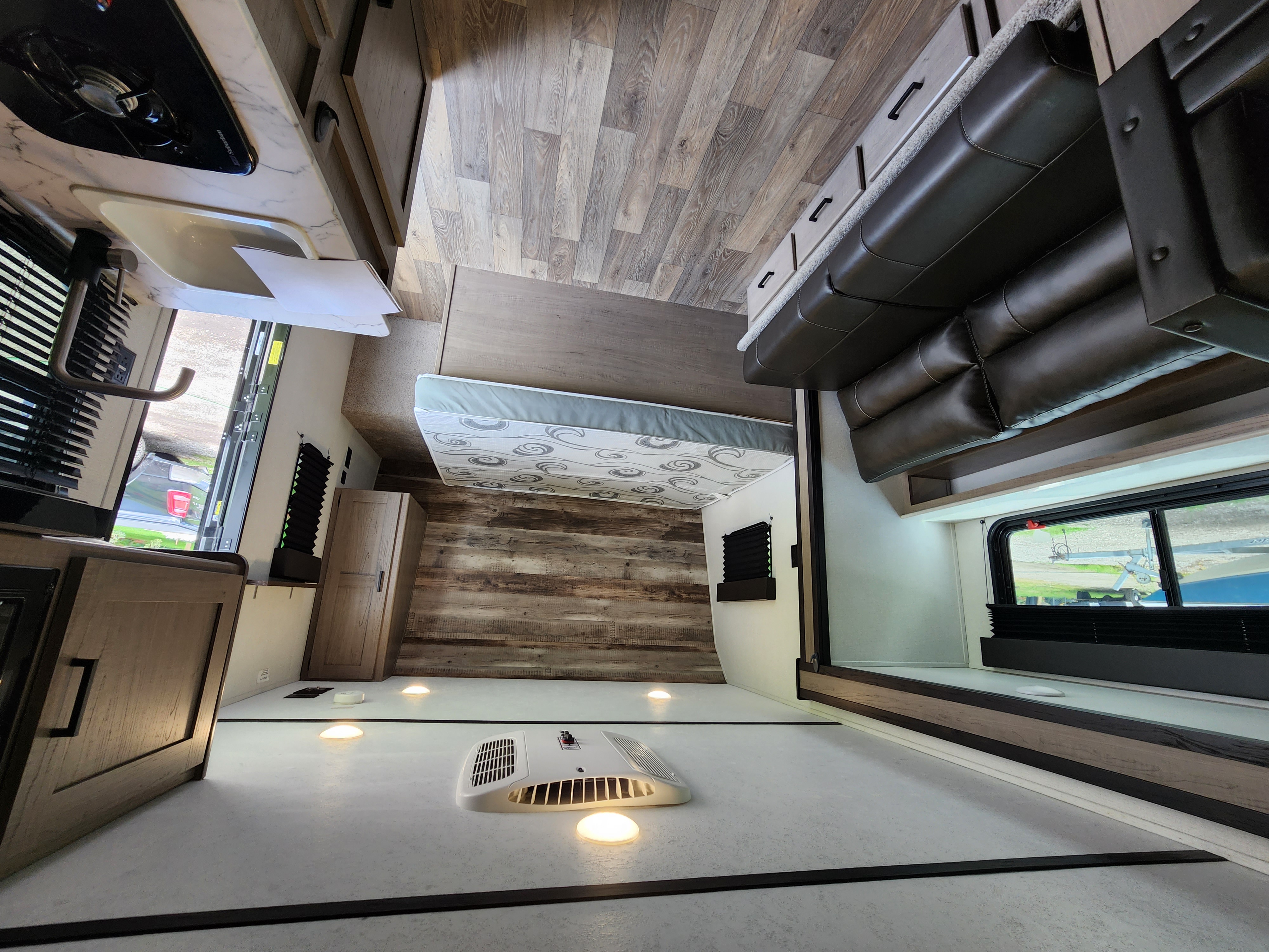 Bright rv rental interior: kitchen counter, patterned bed, and sofa lounge with window view. Modern design, wood flooring.. Keystone RV Hideout 2022