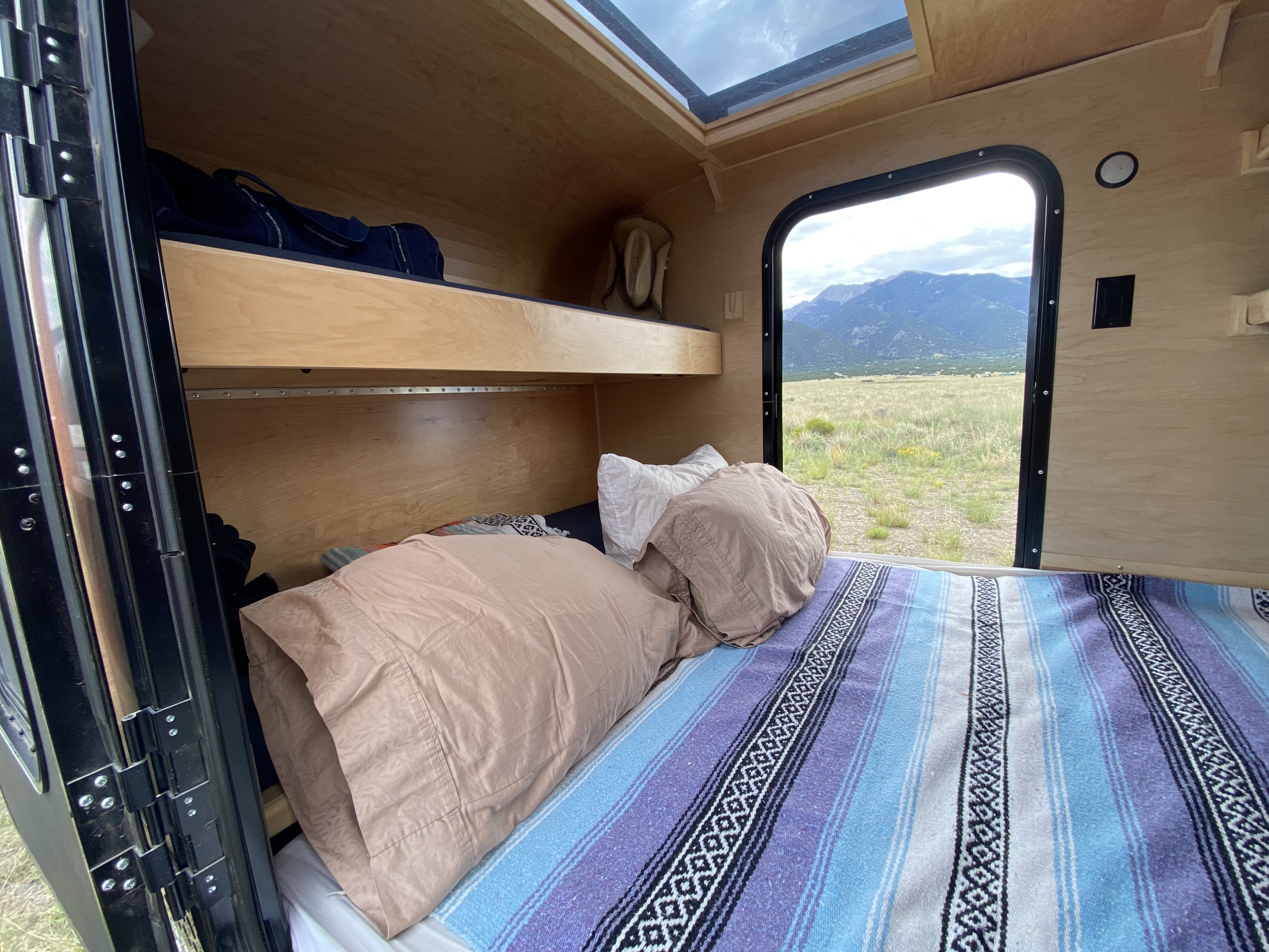 RV rental interior with a comfy bed, bunk, and skylight. Enjoy panoramic mountain views from the large window.. Colorado Teardrop Summit Teardrop 2021