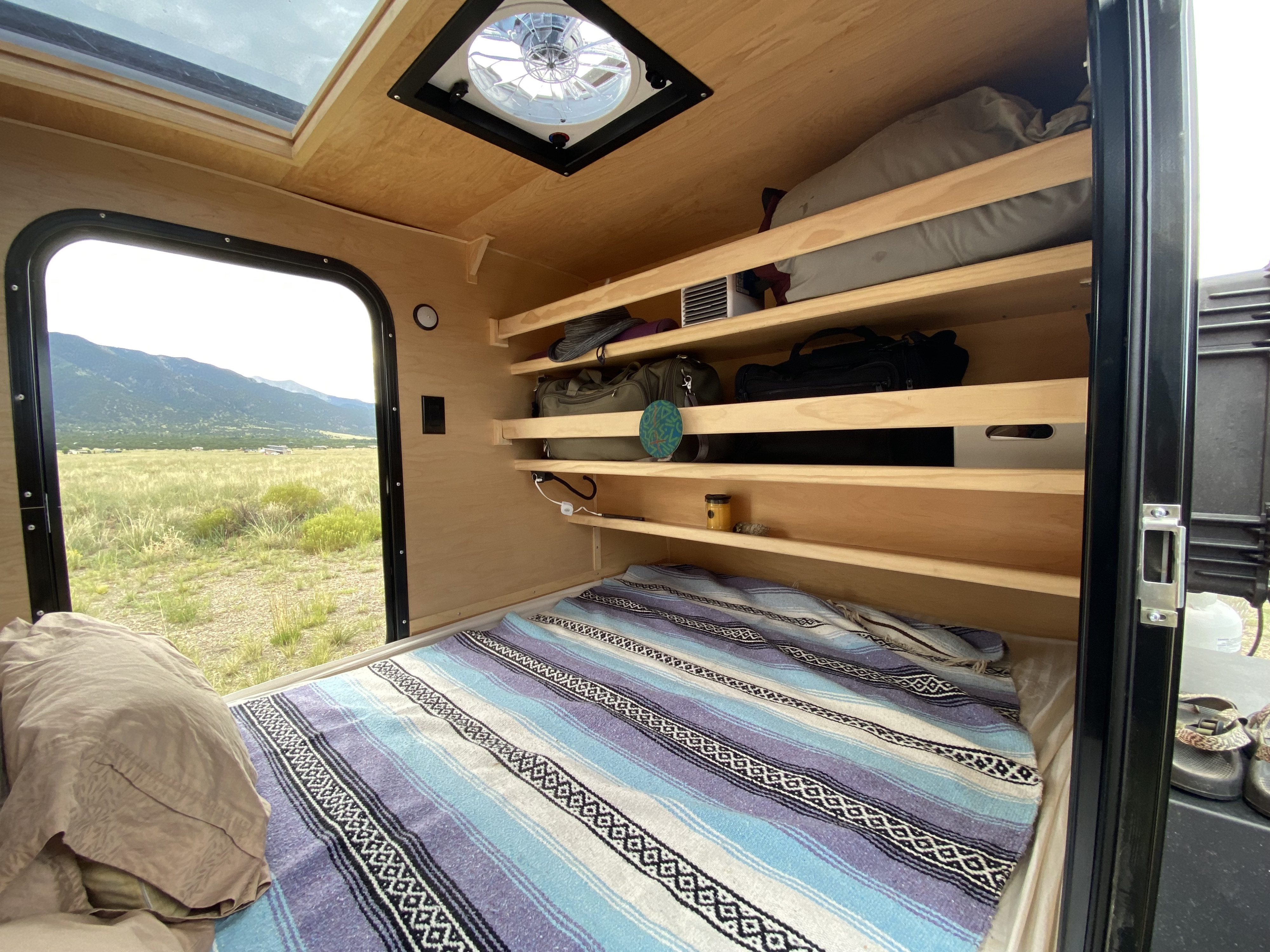 Experience comfort in this RV rental's interior: bed, organized shelves, ceiling vent, & scenic window to mountains.. Colorado Teardrop Summit Teardrop 2021