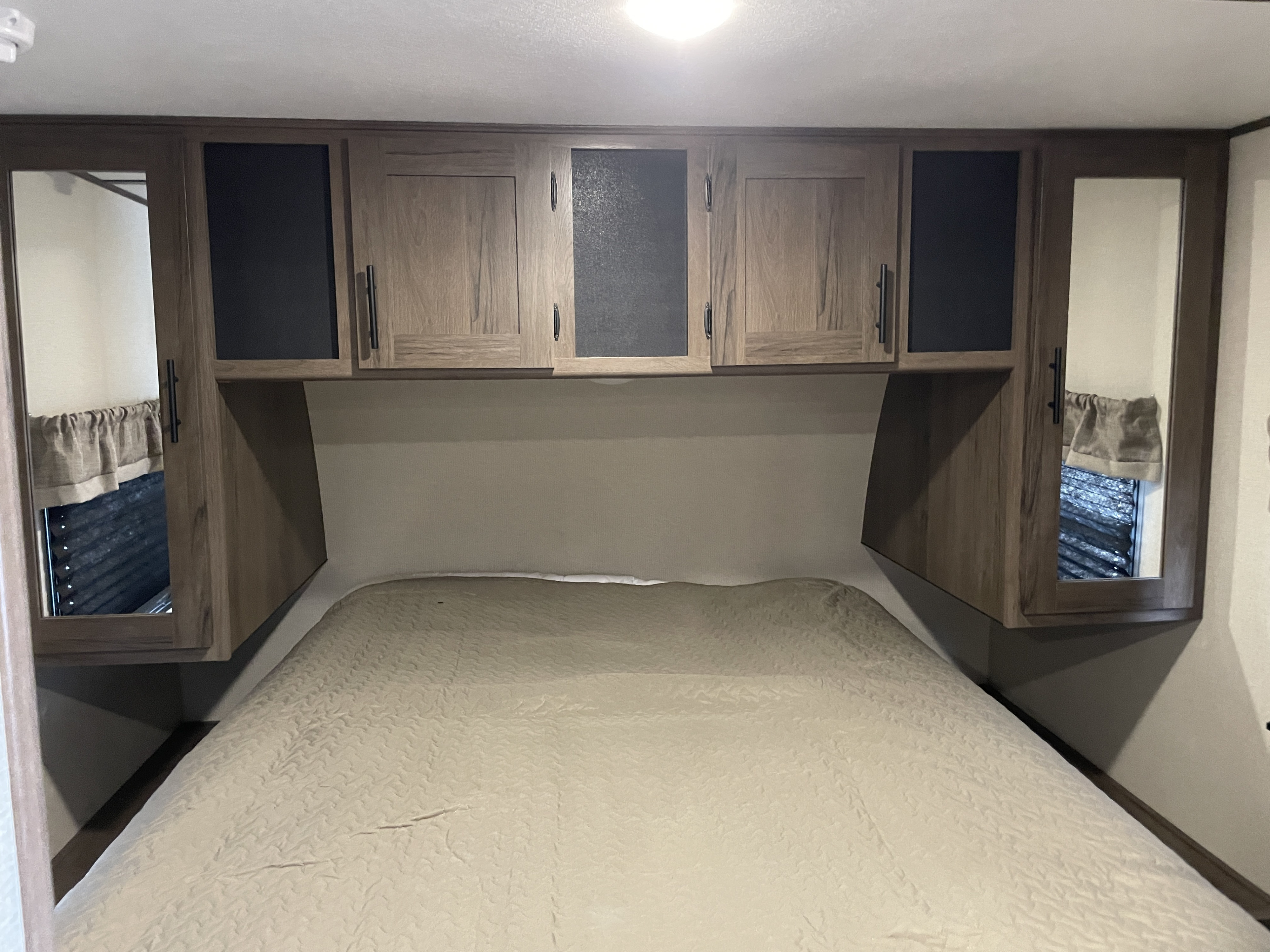 Cozy RV rental bedroom with overhead storage cabinets, a bed, and mirrored closet doors.. Prime Time Avenger 2020