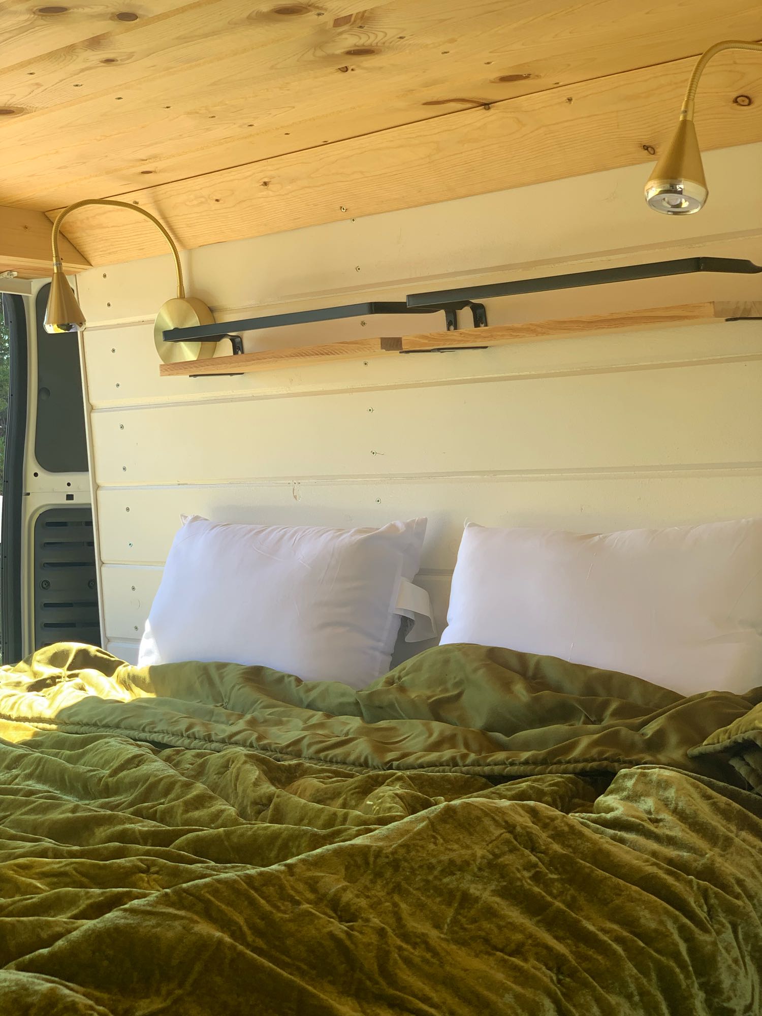 Inside an RV rental: a cozy bed with velvet green bedding, integrated lighting & wood features.. Dodge Promaster 2500 2021