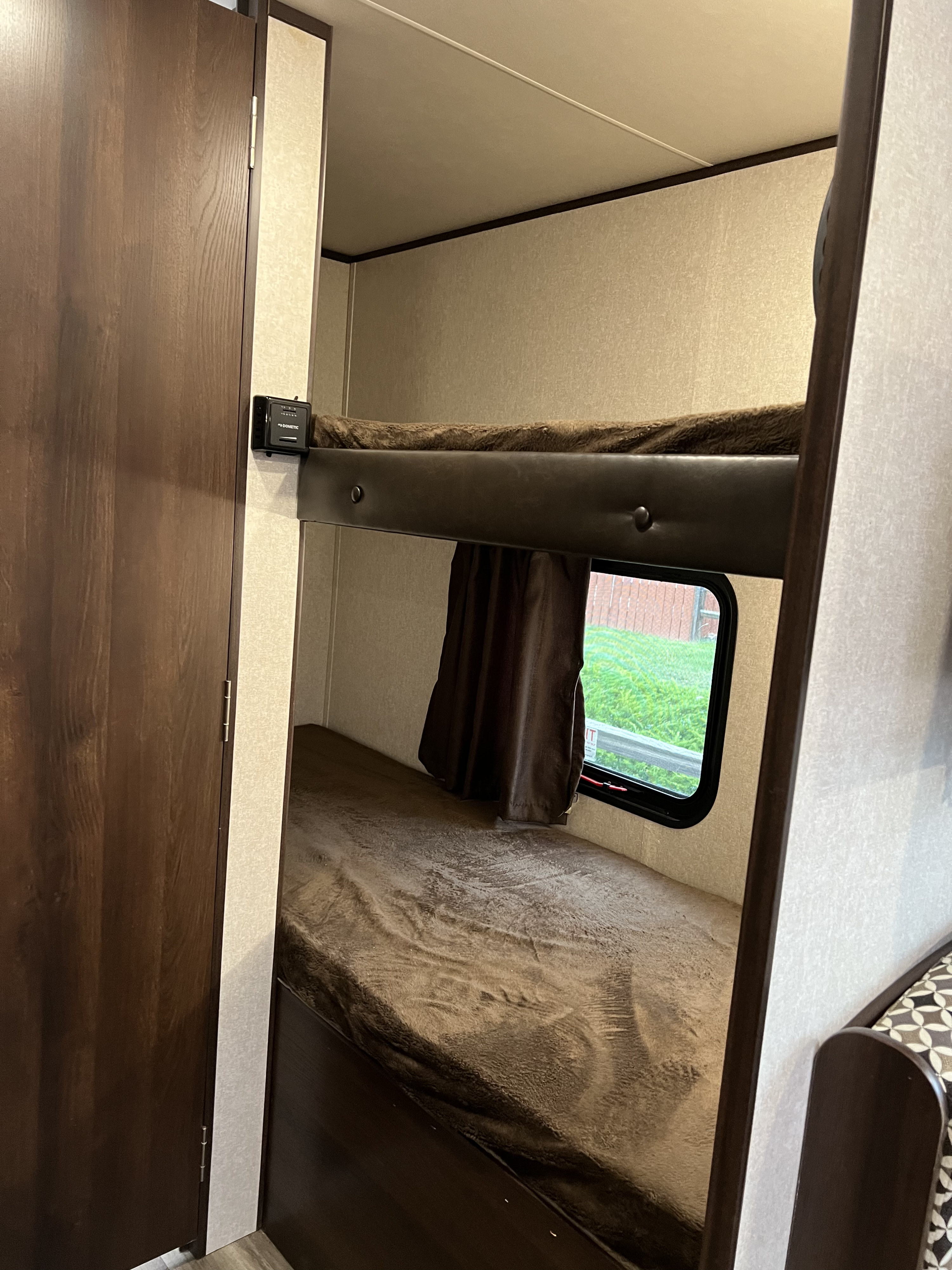RV rental bunk beds with brown bedding, a window showing outside, and a Dometic control panel in an RV interior.. Jayco Jay Flight SLX 2019