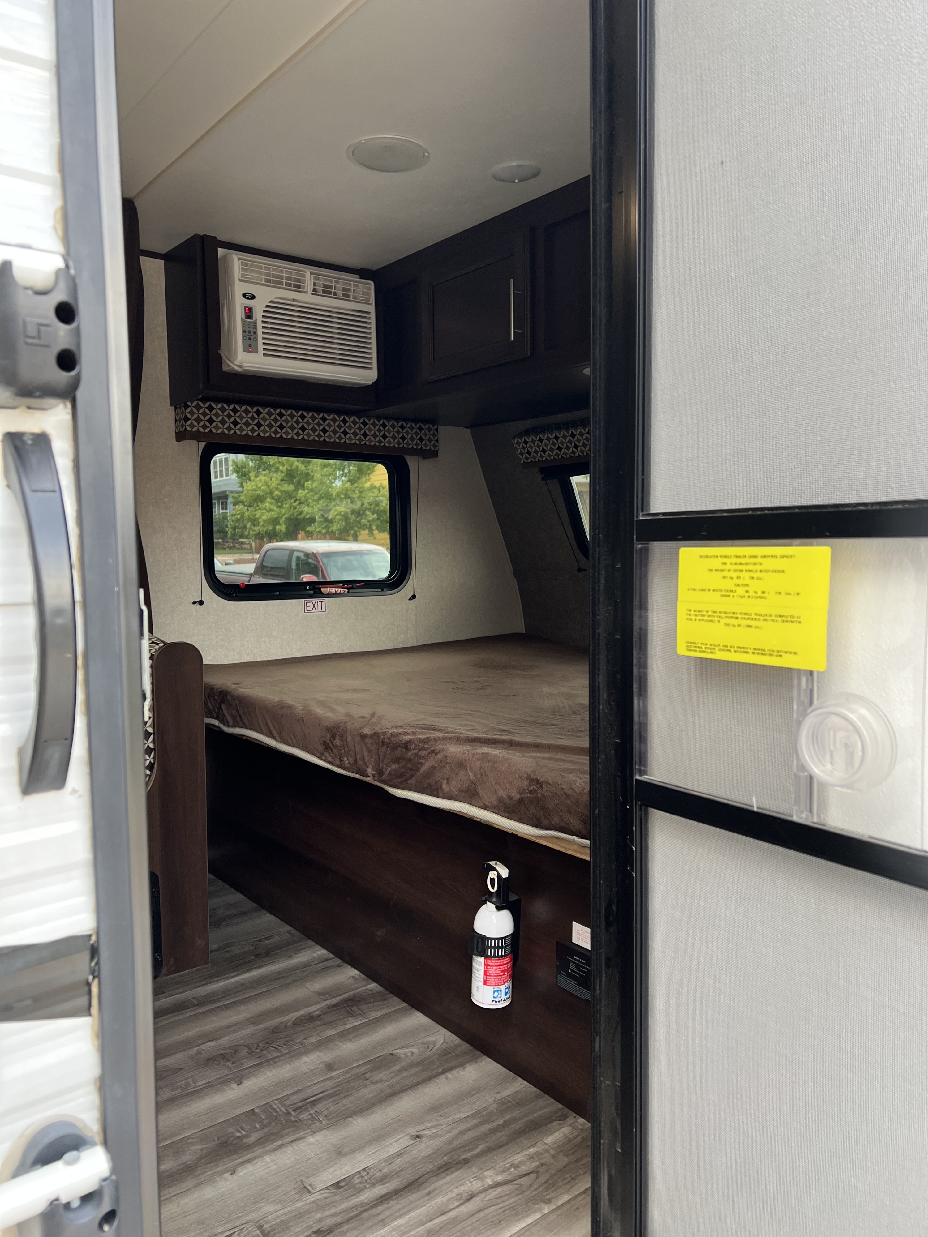 RV rental interior: Bed, window with 'EXIT' sign, AC unit, and fire extinguisher on wood-look floor.. Jayco Jay Flight SLX 2019