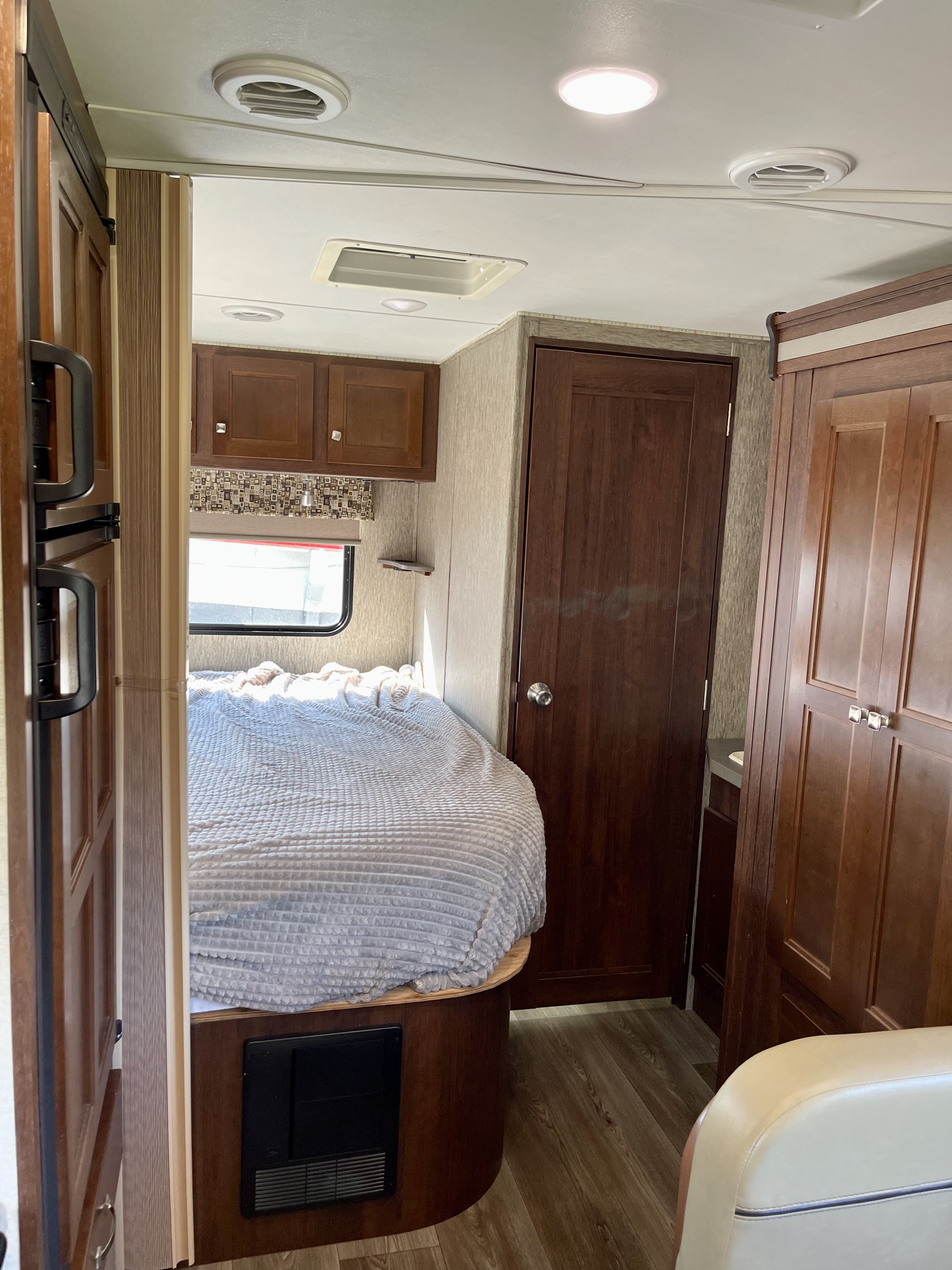 Tour this rv rental's interior! A cozy bedroom features a bed, window, storage cabinets, and a bathroom door.. Forest River Sunseeker 2017