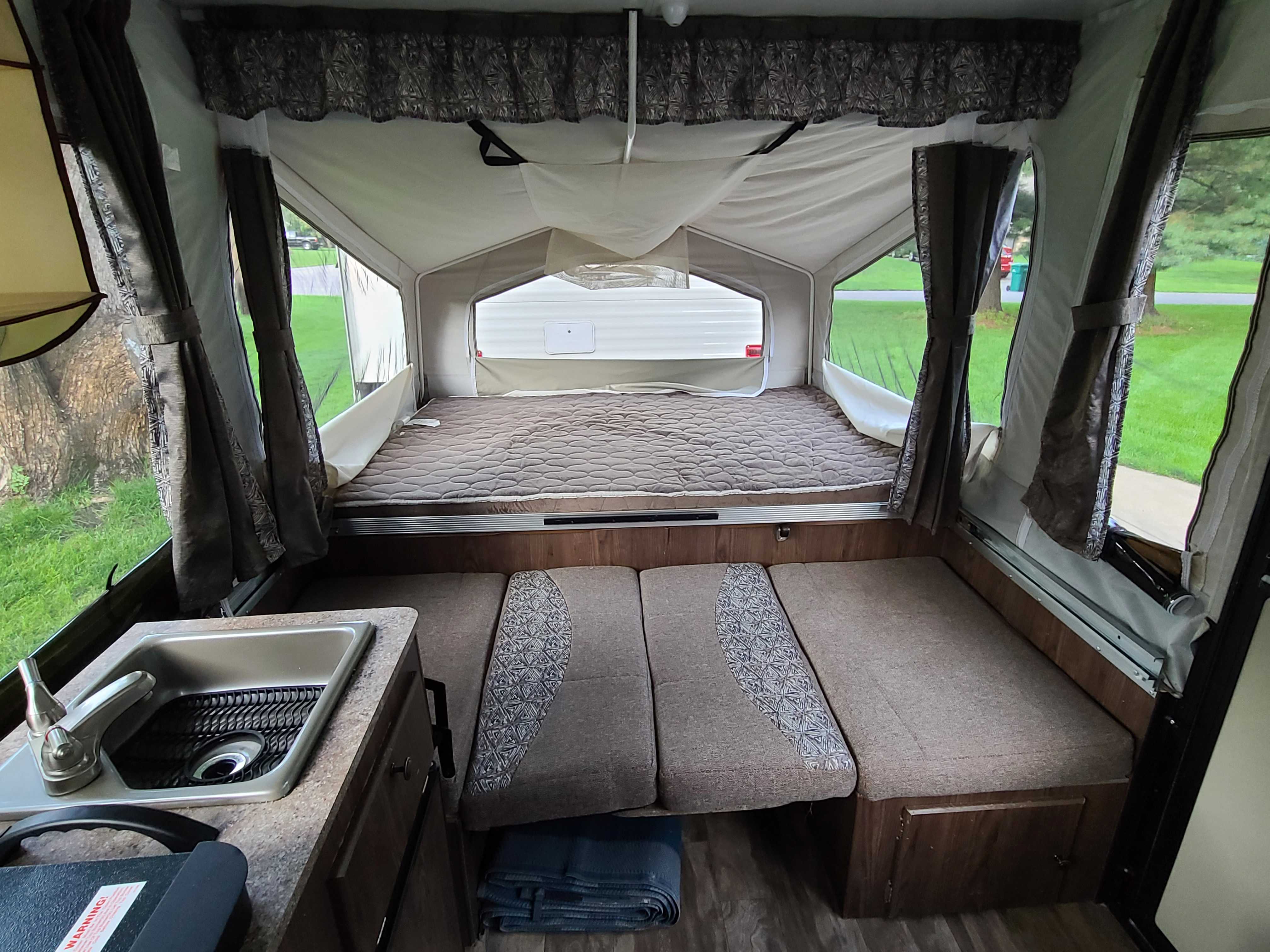 Inside an **rv rental** pop-up camper: a cozy bed, convertible dinette seating, and a compact sink area. Ideal for travel.. Forest River Flagstaff M.A.C. 2019