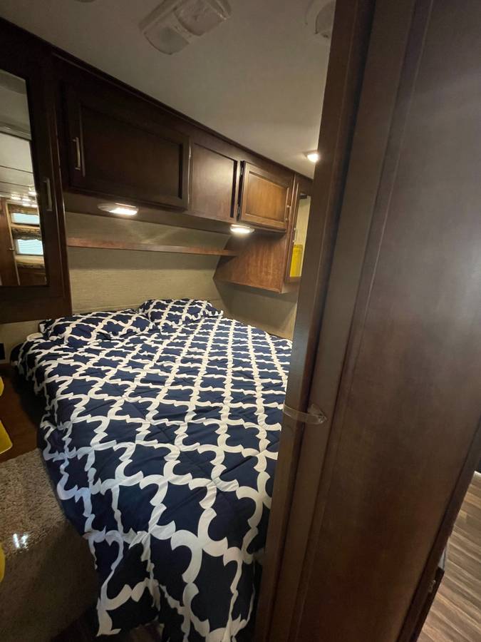 Compact RV rental bedroom featuring dark wood storage, a bed with blue/white comforter, and built-in lighting. Ideal for road trips.. Keystone RV Outback Ultra-Lite 2016