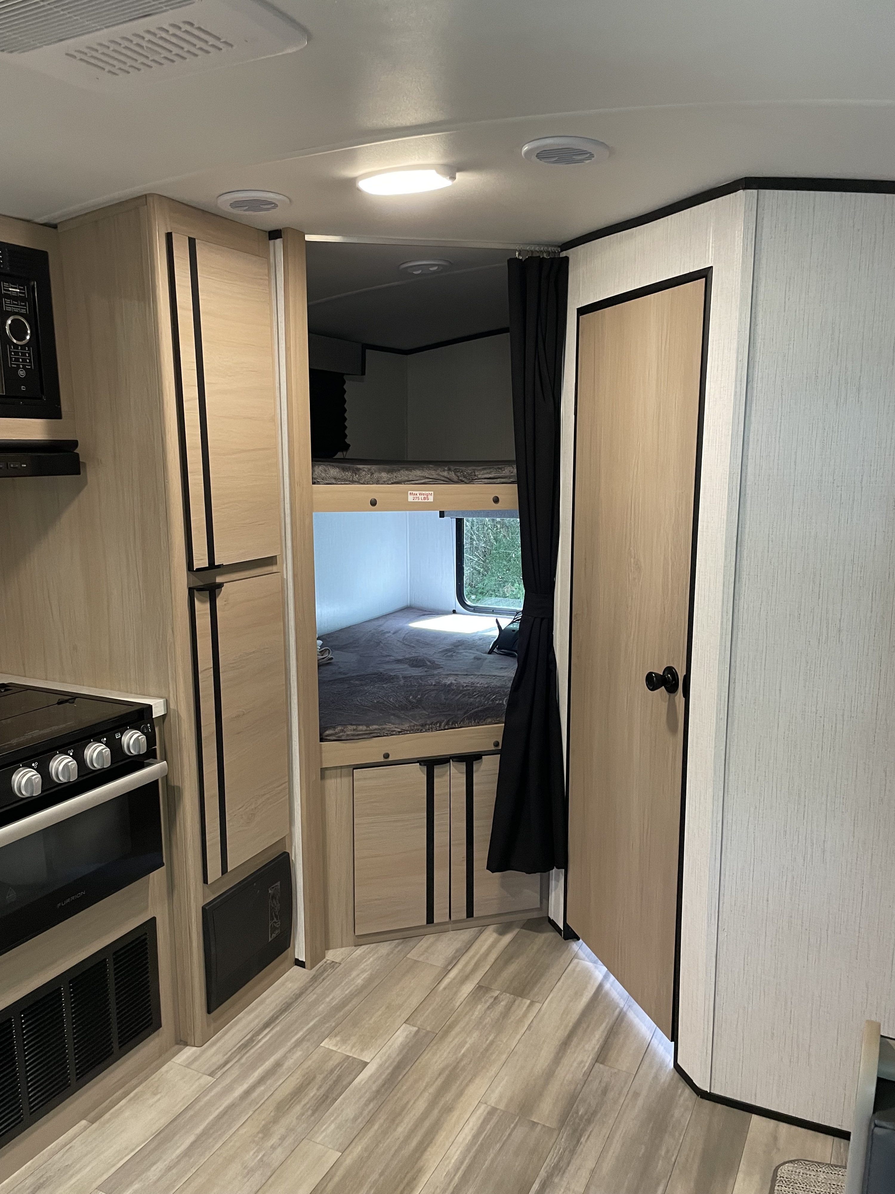 RV rental interior: Kitchen with appliances on the left, next to cozy bunk beds, featuring light wood cabinets and flooring.. Cruiser Rv Corp Radiance 2022