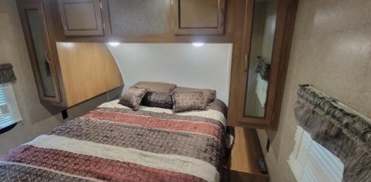 RV rental interior: A cozy bedroom featuring a patterned bed, overhead lights, and built-in wood cabinets for comfortable travel.. Coachmen Catalina 2019