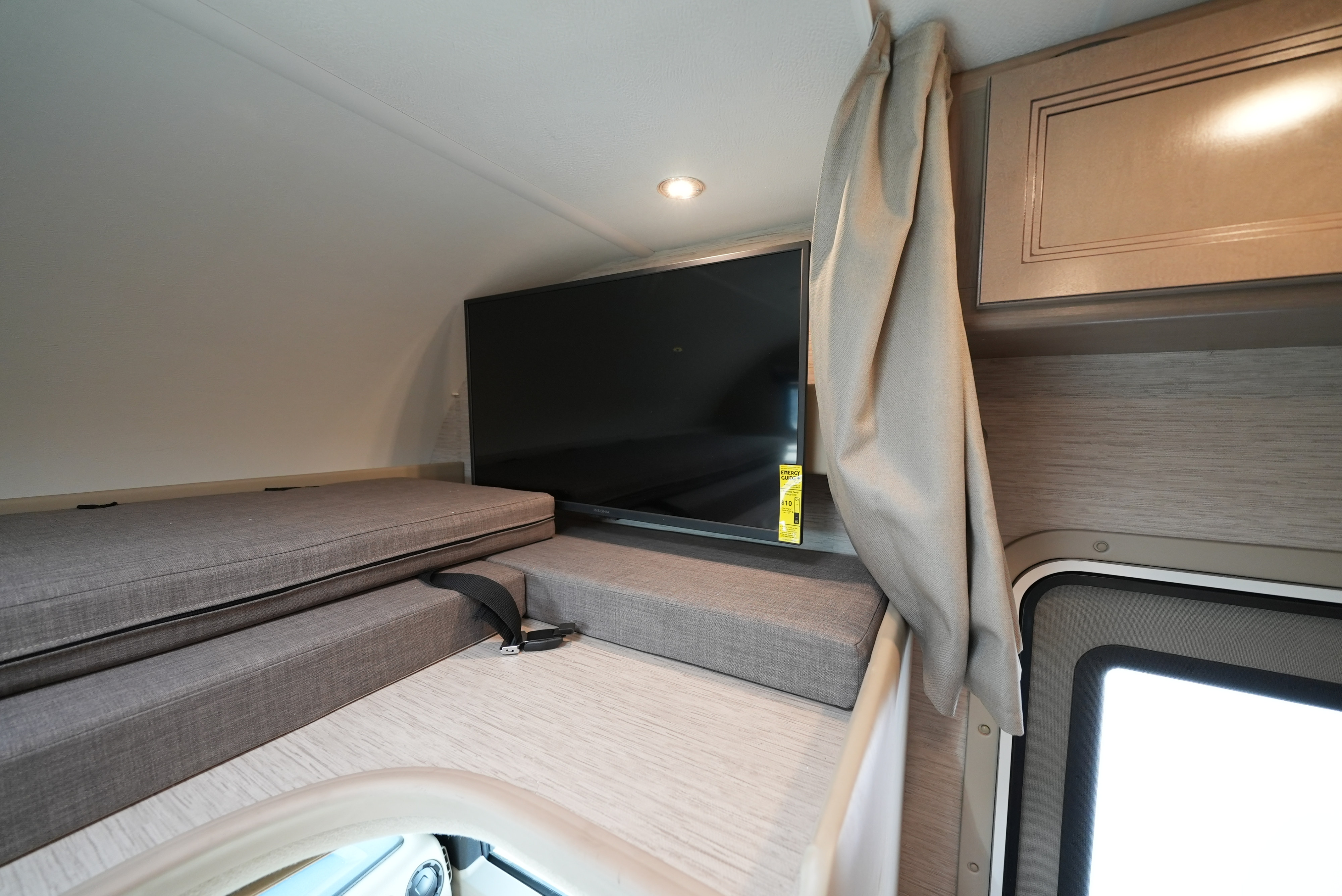 This RV rental shows a cozy interior: a flat-screen TV, upholstered bed/seating, an overhead cabinet, and a window with curtain.. Thor Motor Coach Four Winds 2023