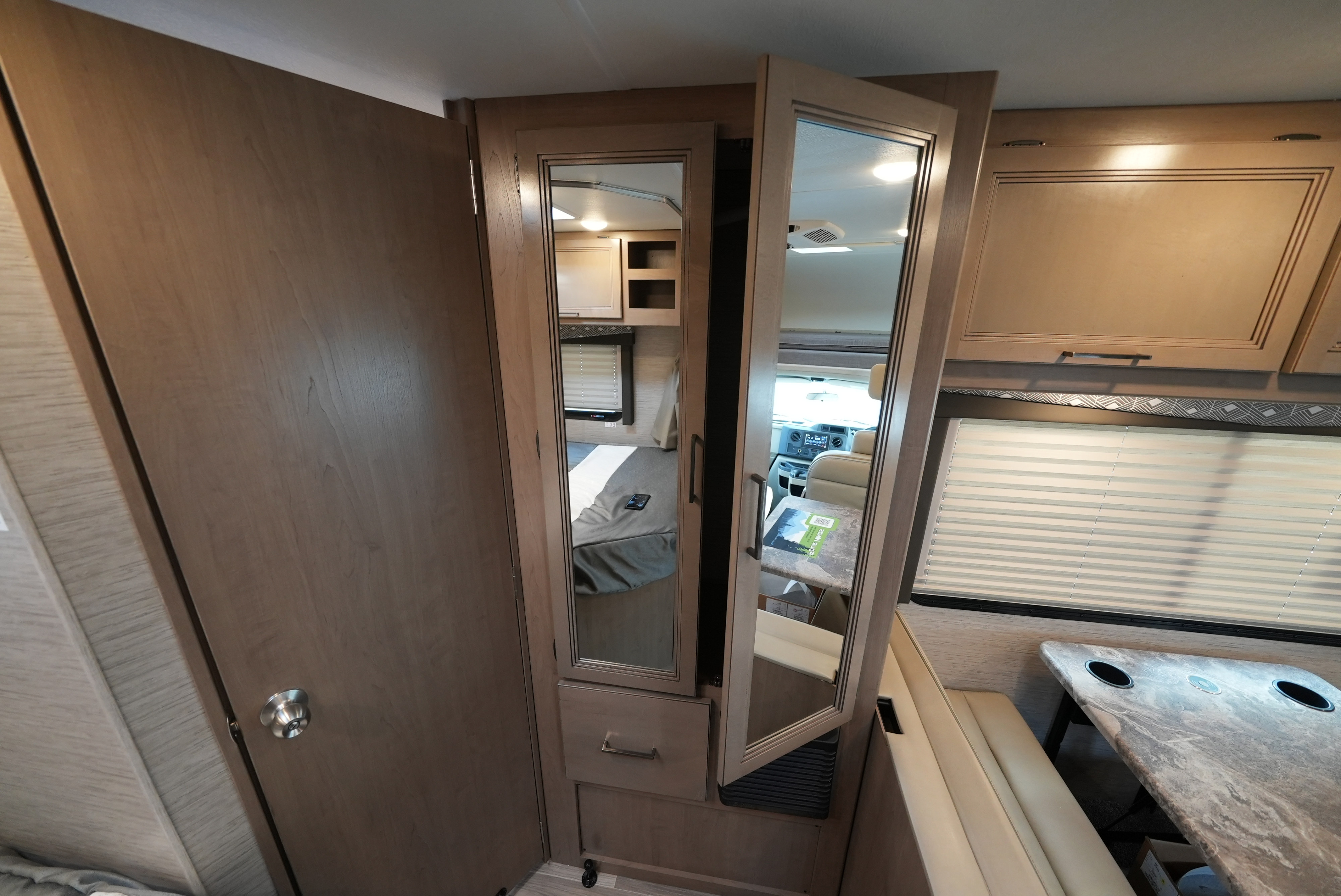 Inside an RV rental: Mirrored cabinet doors reveal the bedroom and cab, alongside a comfortable dinette.. Thor Motor Coach Four Winds 2023