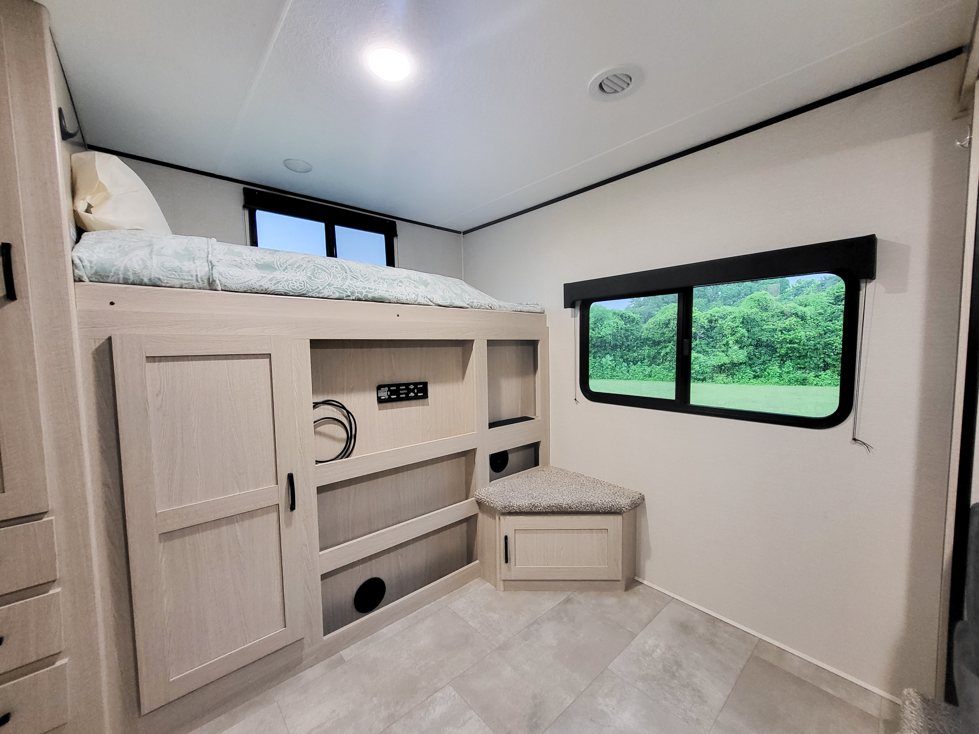 Modern rv rental interior: bunk bed with light bedding, built-in storage, and a window framing nature views.. Coachmen Apex 2021