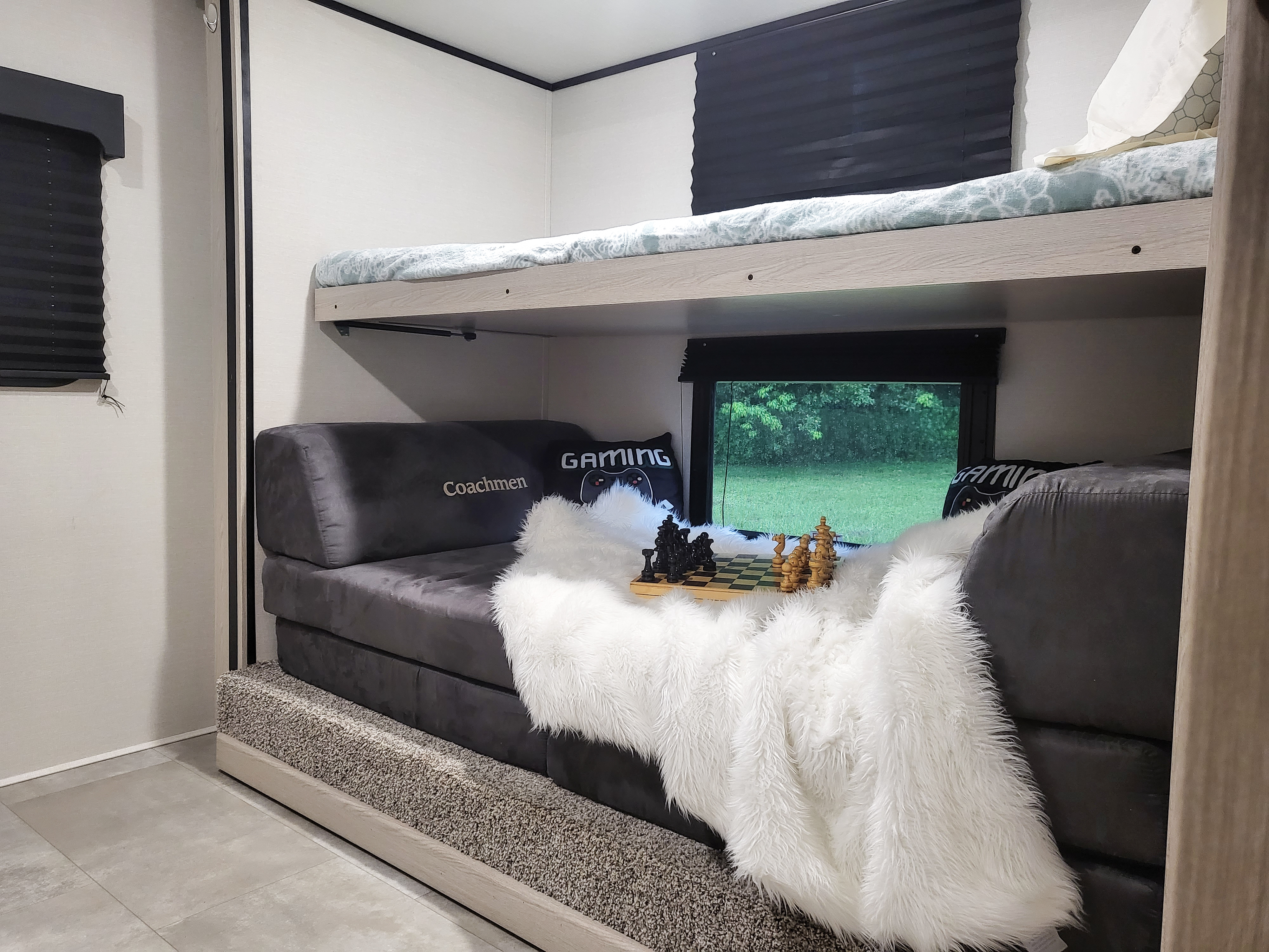 RV rental features a bunk bed over a sofa with a chess set, gaming pillow, and window view. Ideal for travel.. Coachmen Apex 2021