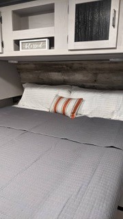 This comfortable RV rental bedroom features a bed with white and striped pillows, a rustic headboard, and functional overhead cabinets.. Heartland RVs Mallard 2022