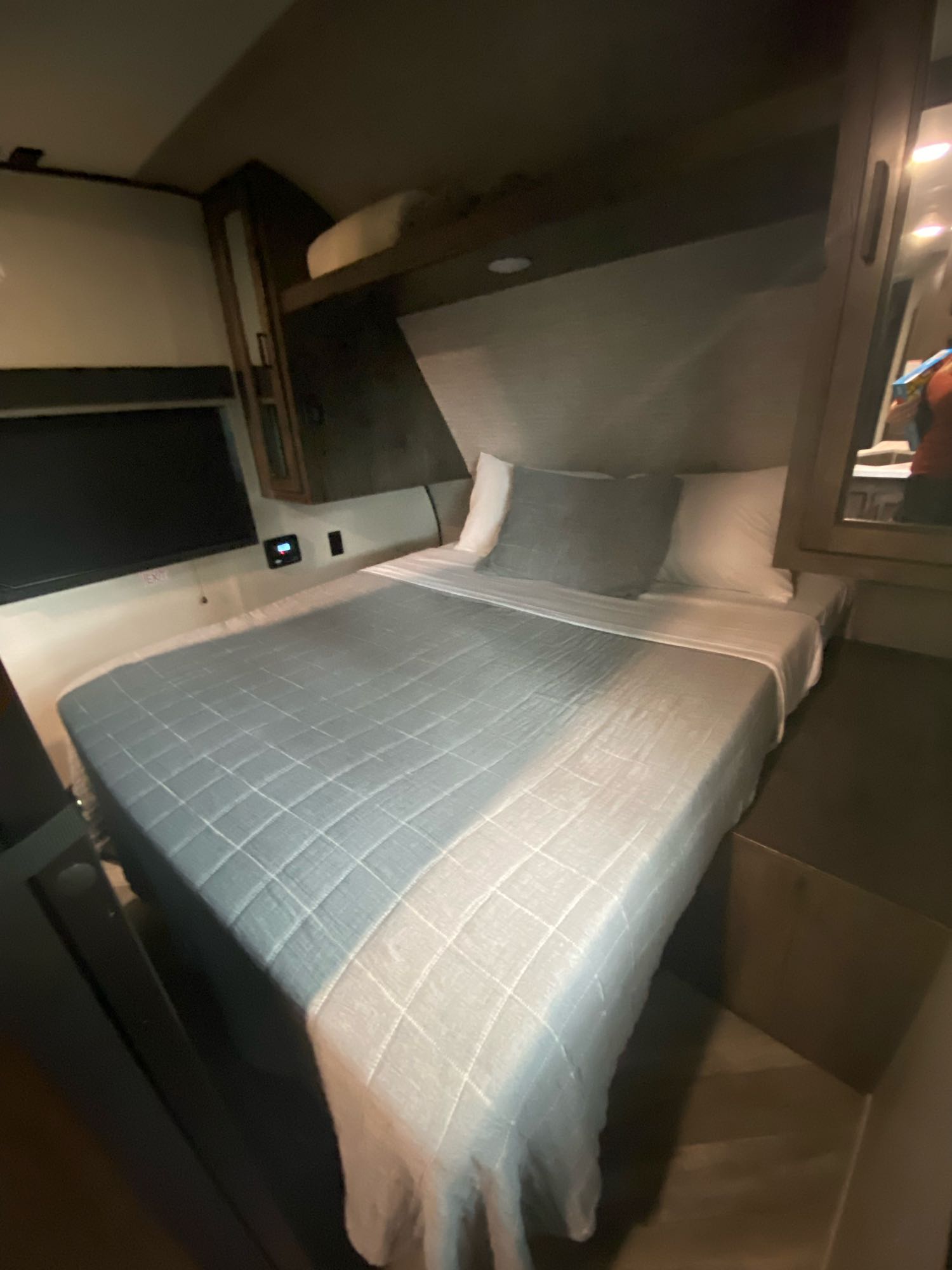 Cozy RV rental bedroom featuring a comfy bed with a quilted cover, wall-mounted TV, and overhead storage.. Highland Ridge Olympia 2022