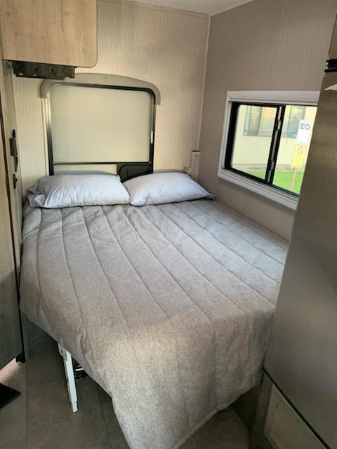 A comfortable rv rental bedroom, featuring a compact bed with grey bedding, pillows, and a window, ready for a restful sleep.. Forest River Coachmen Cross Trail XL 2022