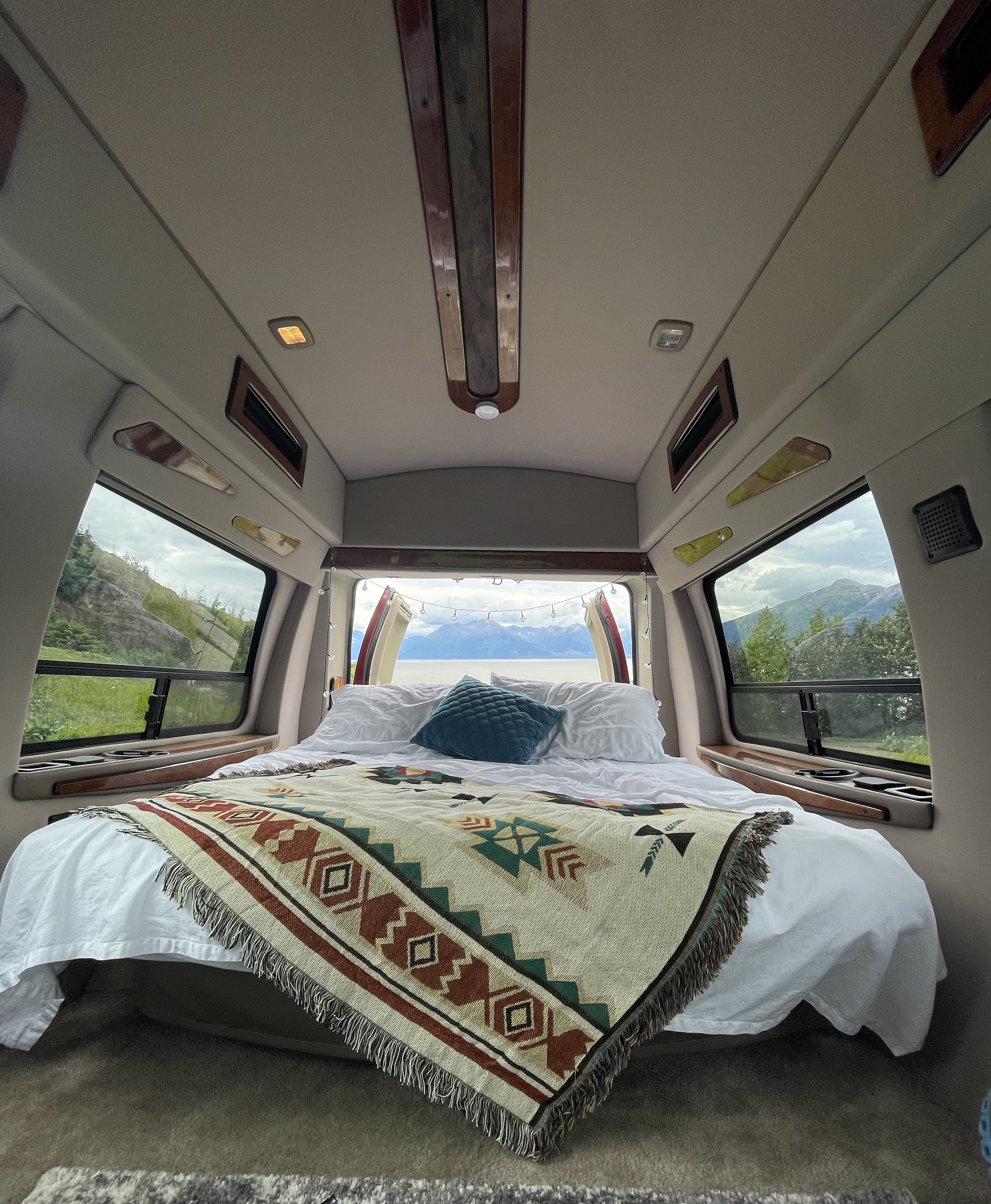 Cozy rv rental interior featuring a comfy bed with a patterned blanket and stunning mountain & lake views out the back.. Ford Econoline 150 1999