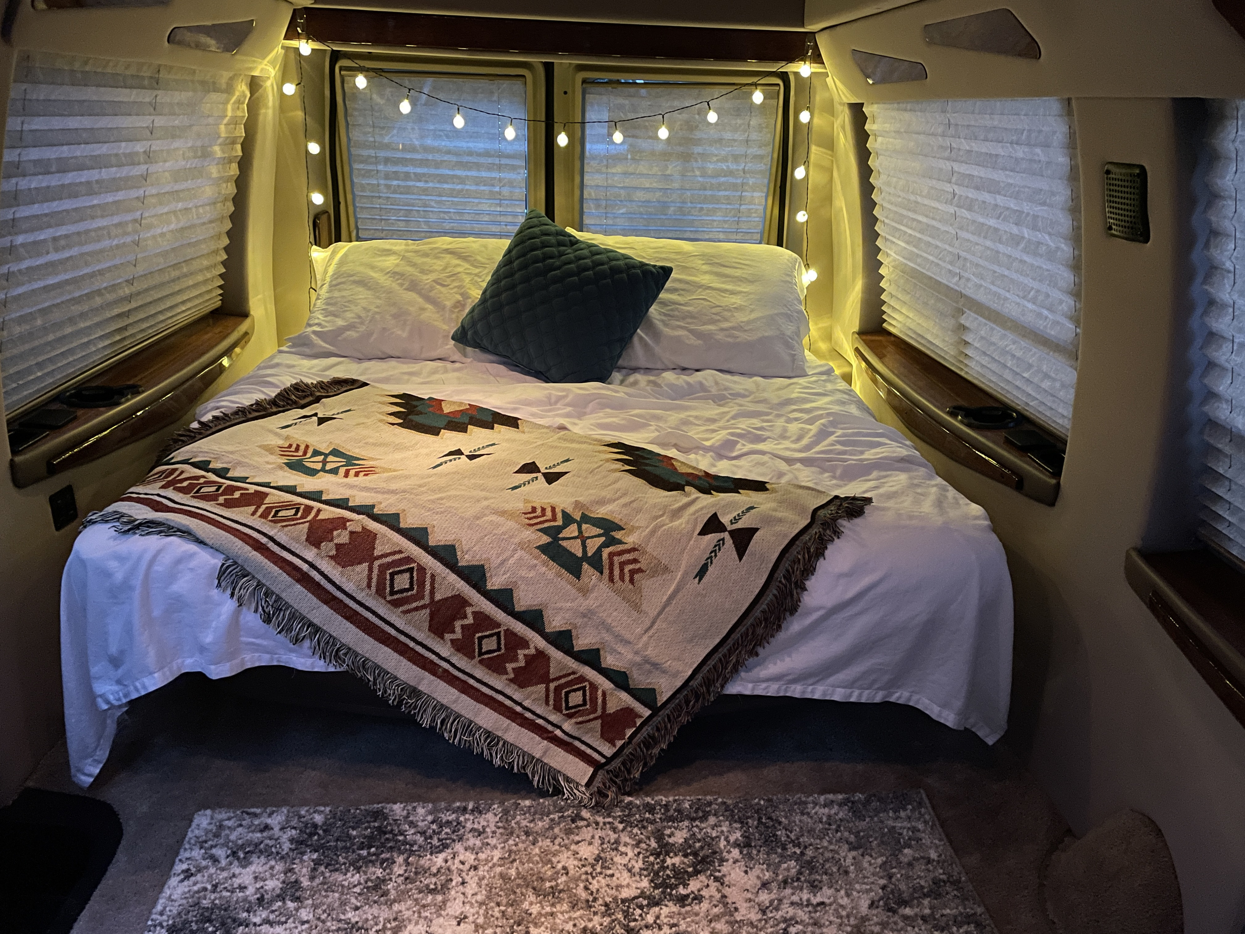 Inviting RV rental bedroom with a comfy bed, Southwestern blanket, ambient string lights, and pleated window blinds.. Ford Econoline 150 1999