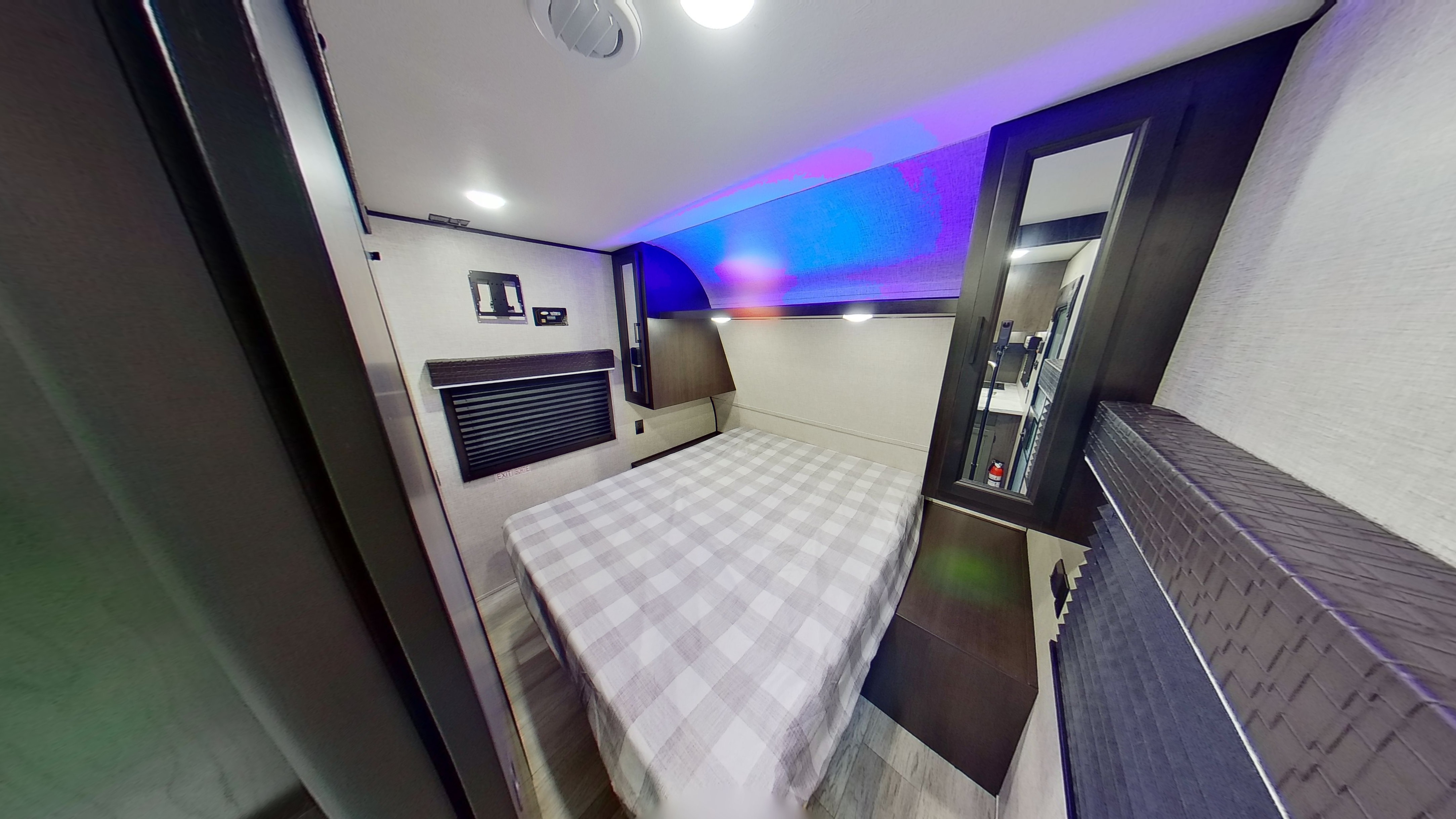 Interior of an RV rental bedroom showing a plaid-covered bed, window, wall-mount TV bracket, and blue/purple LED lighting.. Jayco Jay Flight 2022