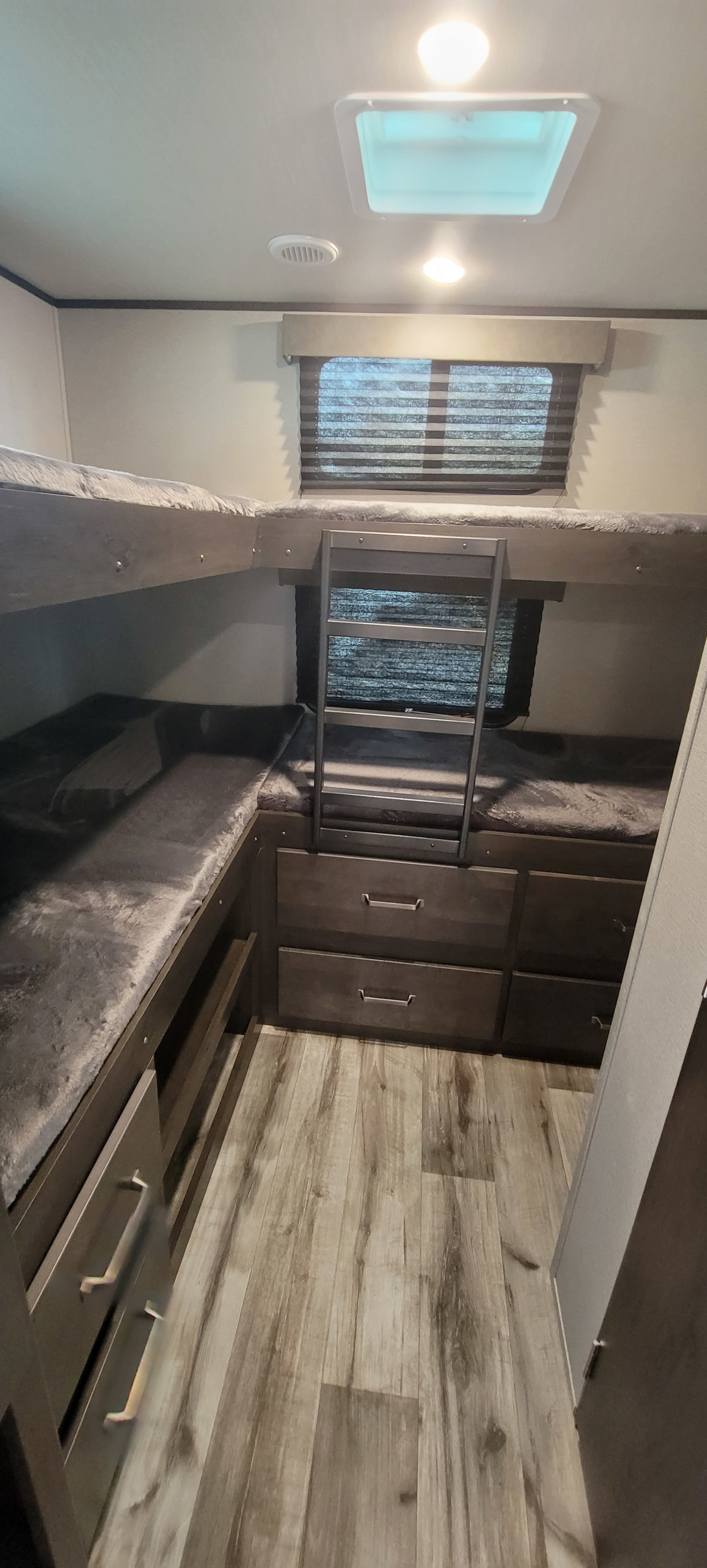 This RV rental features cozy bunk beds with soft gray bedding, built-in storage drawers, a ladder, and a window for comfort.. Grand Design Transcend 2022
