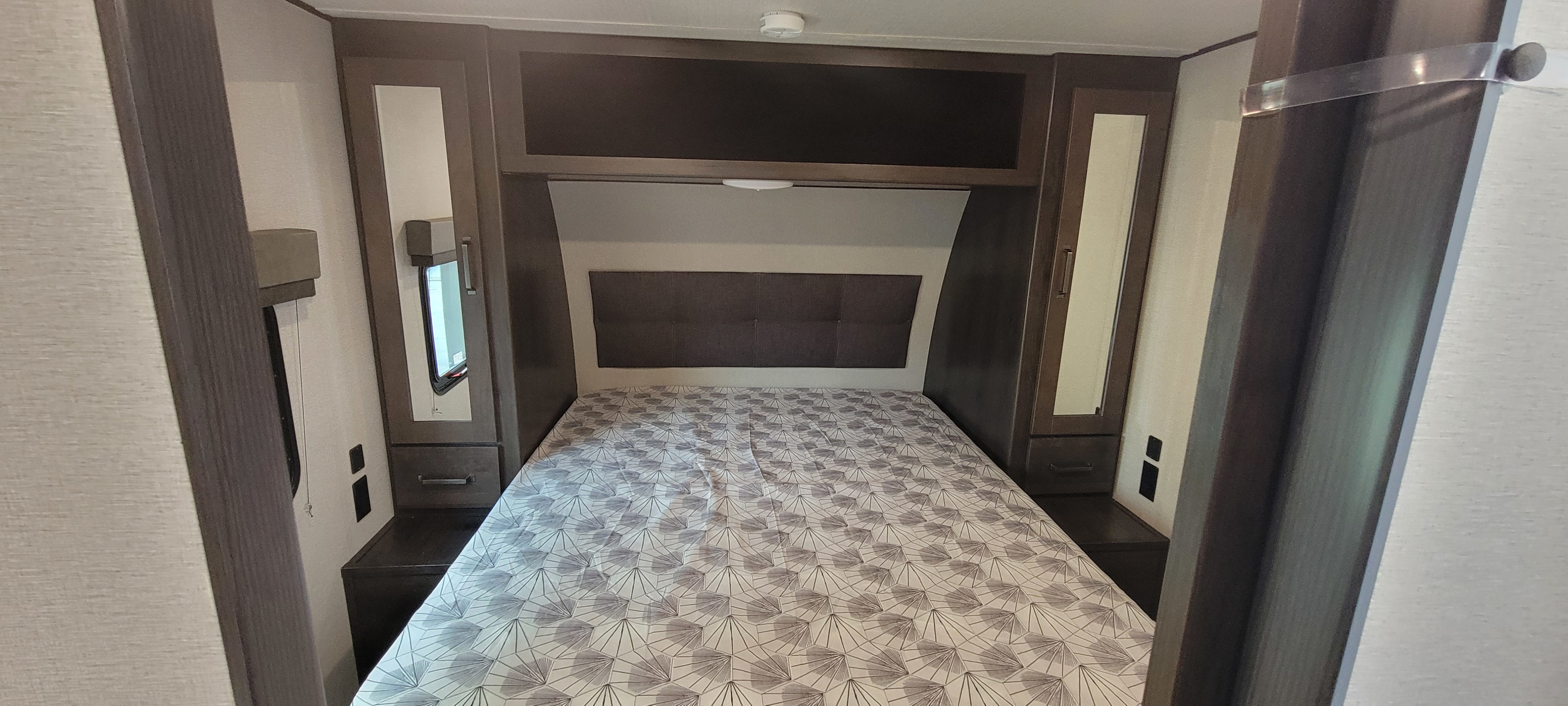 Cozy RV rental bedroom featuring a patterned comforter, overhead storage, and mirrored wardrobes with nightstands.. Grand Design Transcend 2022