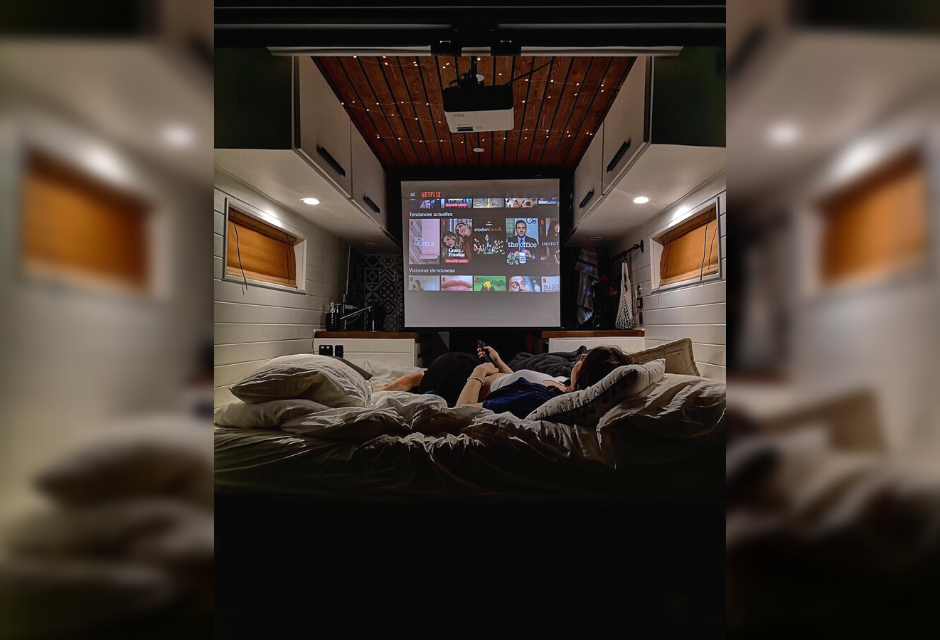 Cozy RV rental: person watches Netflix on a projector screen in a comfortable custom van.. RAM Promaster 2500 2017