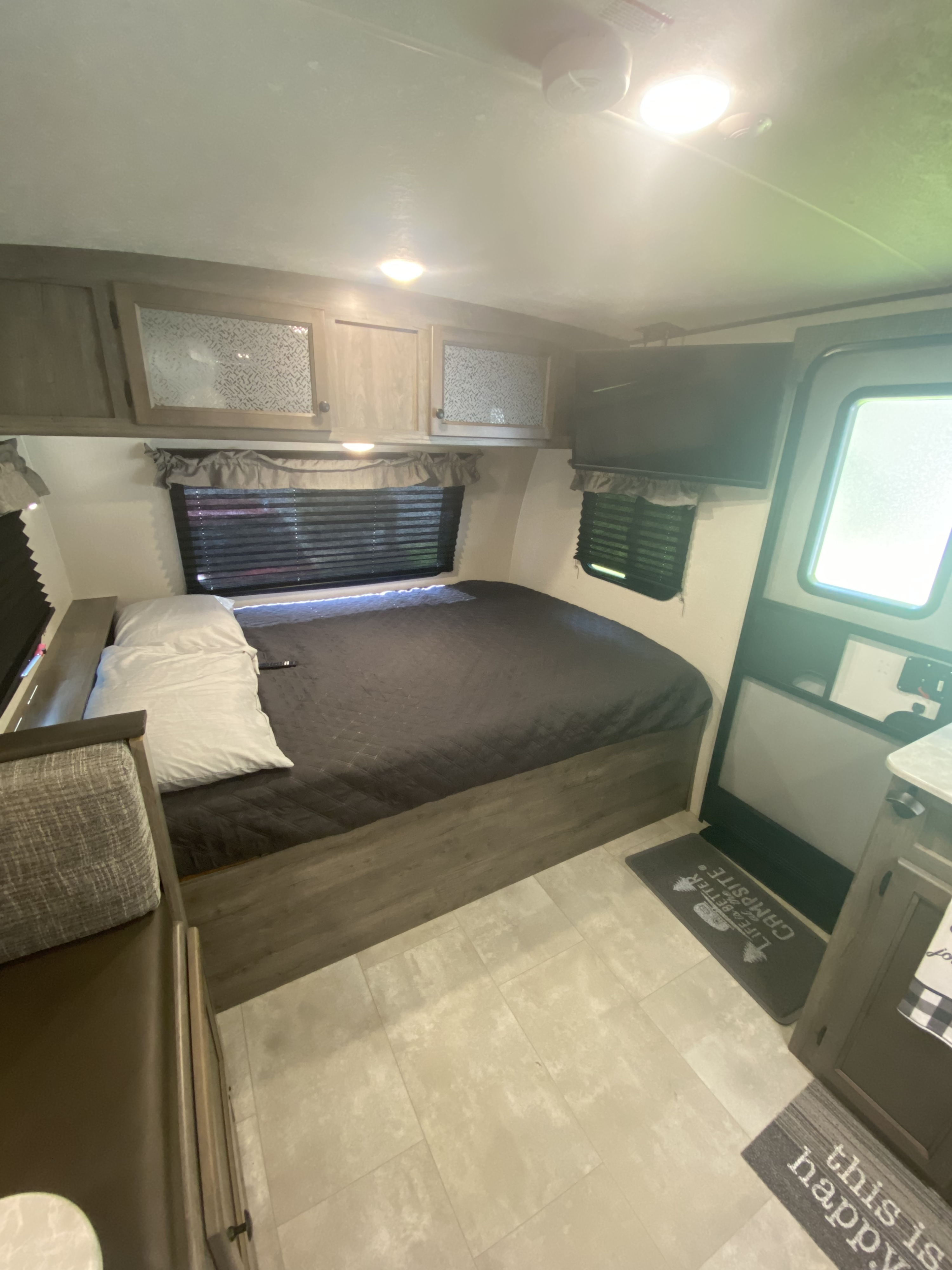 RV rental interior: cozy bedroom with bed, overhead cabinets, wall-mounted TV, and blinds. Ready for adventure.. Coachmen Apex Nano 2021