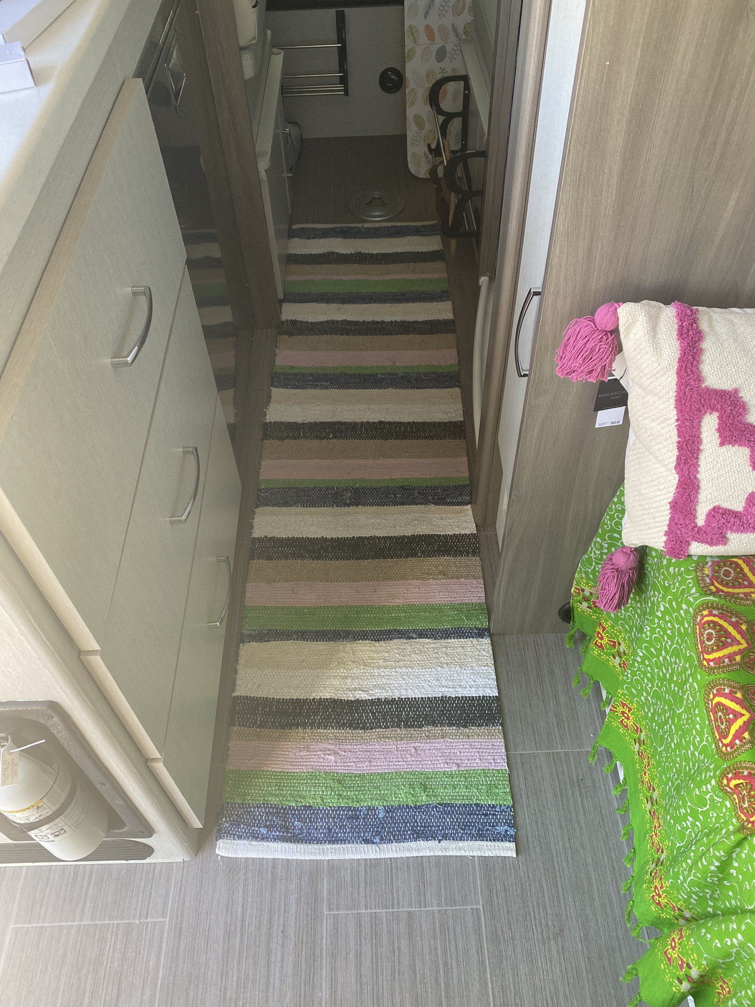 RV rental interior: A striped rug lines the hallway, flanked by light wood cabinets and a colorful bedding area leading to the bathroom.. Thor Tellaro 2022