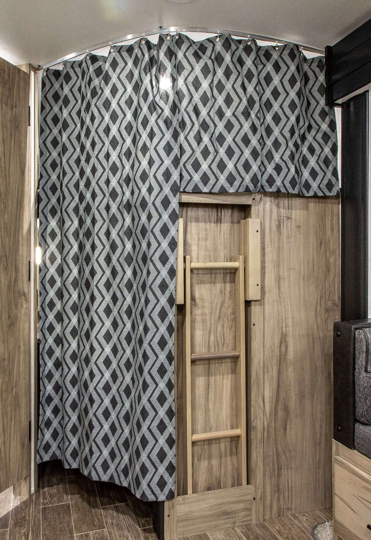 Inside an RV rental: view of a gray diamond-patterned privacy curtain for bunk beds with a wooden ladder. Ideal for travel.. Forest River Alpha Wolf 26DBH-L 2021