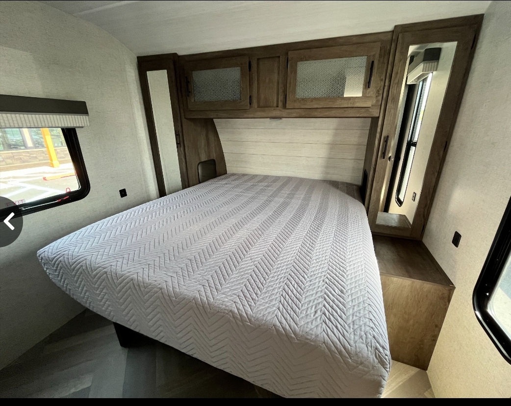 Comfortable RV rental bedroom featuring a full-size bed with light gray quilt, overhead cabinets, and mirrored closets.. Forest River Salem 2021
