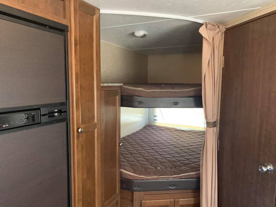 RV rental bunkhouse: shows stacked beds with brown quilts, an RV fridge, and wood cabinetry.. Keystone RV Hideout Luxury 2015