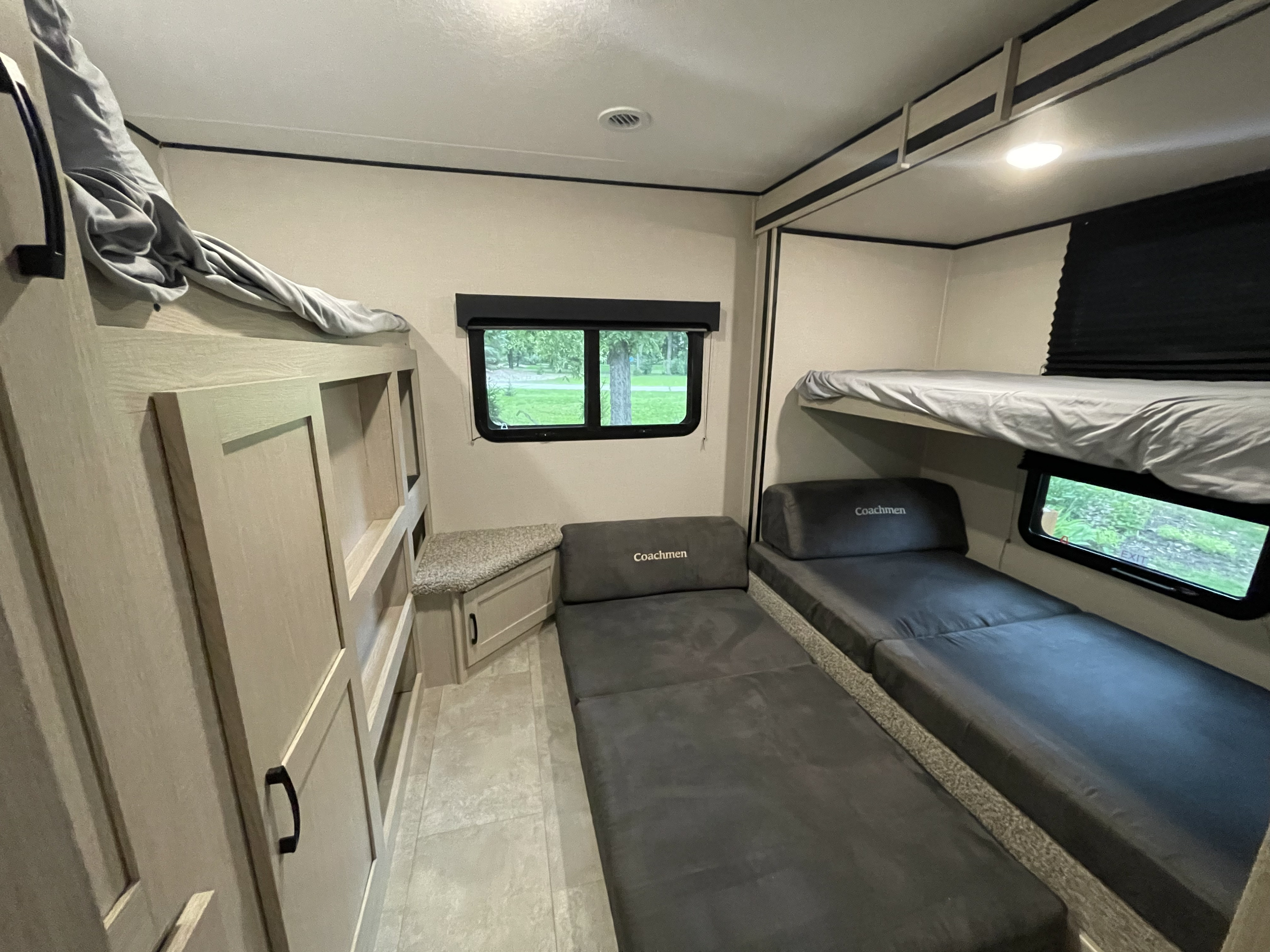An RV rental bunkroom shows three beds: two lower "Coachmen" cushion beds and an upper bunk. Built-in storage included.. Coachmen Apex 2021