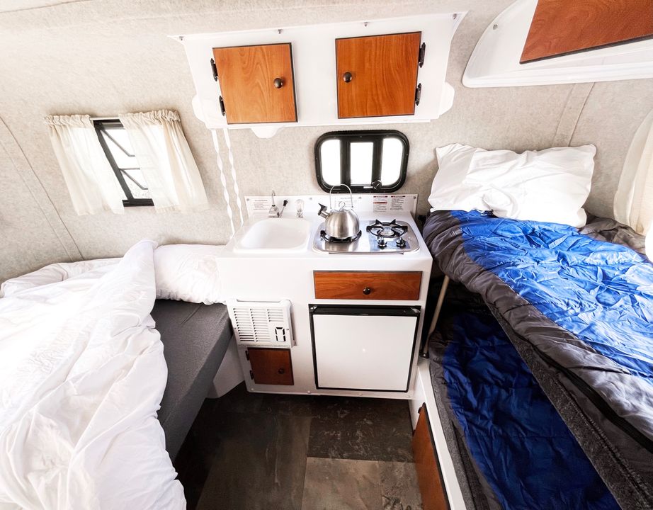 Cozy RV rental interior featuring a compact kitchen (sink, stove, fridge) and two single beds. Ideal for travel adventures.. Scamp Scamp Trailer 2018