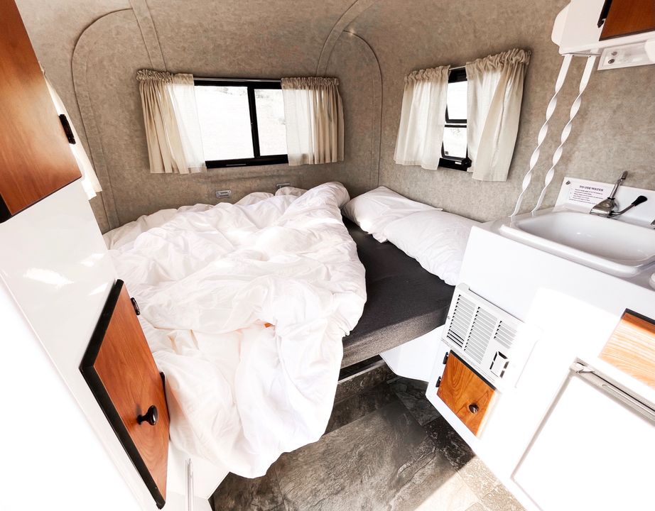 Compact rv rental interior with a cozy bed, white bedding, small sink, and windows providing natural light.. Scamp Scamp Trailer 2018
