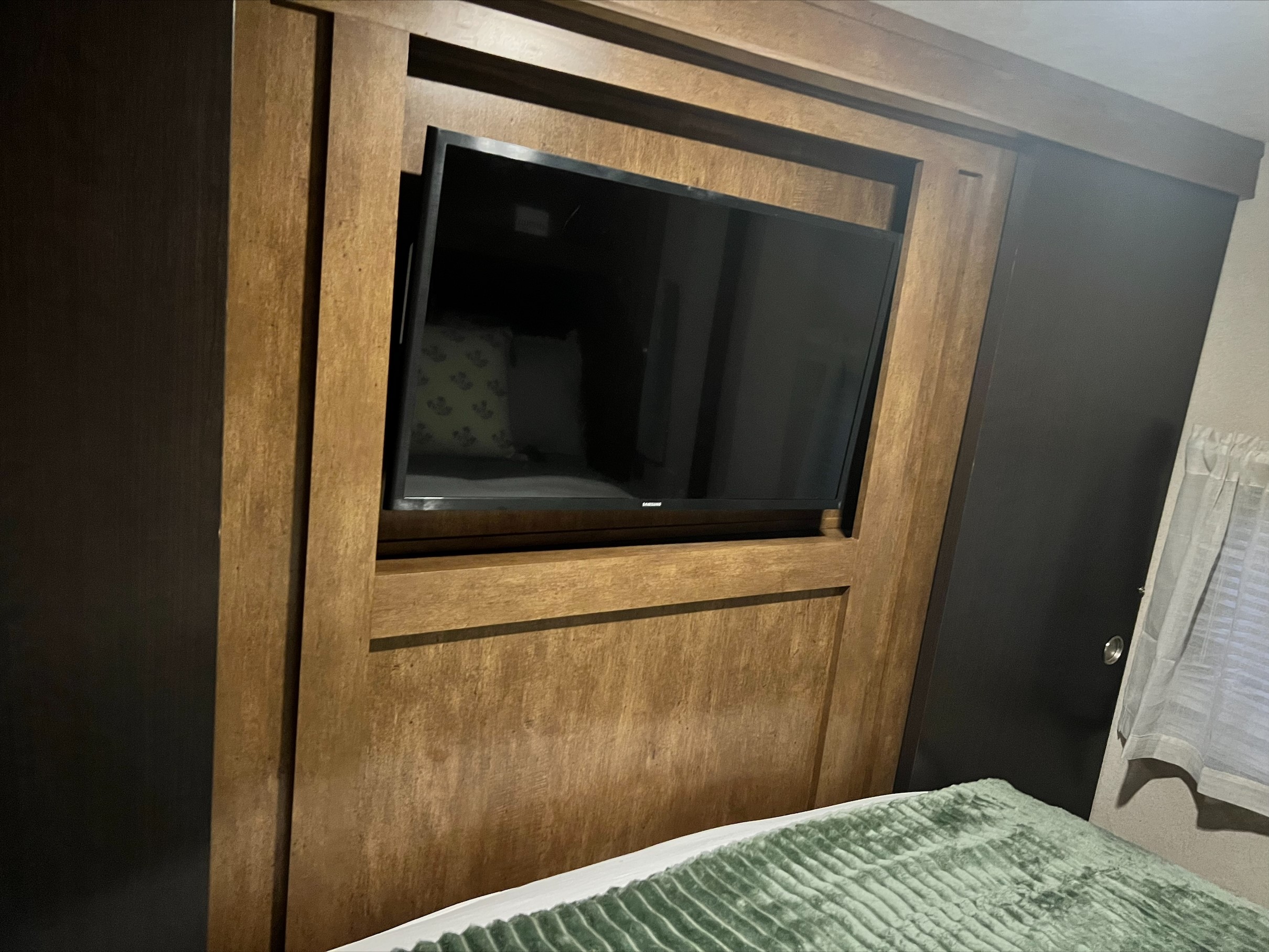 RV rental: A flat-screen TV is built into wooden wall cabinetry in a bedroom, with a green blanket on the bed foreground.. Forest River Wildwood 2017