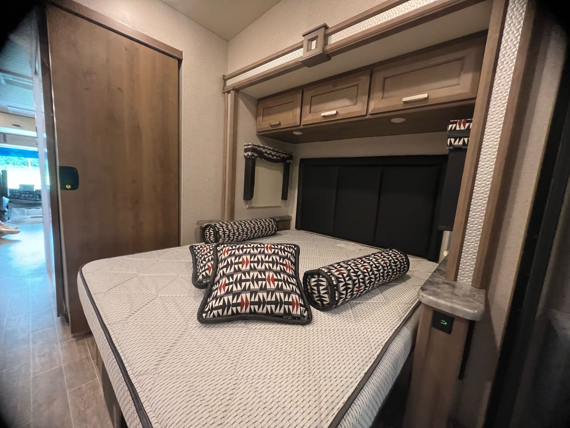 RV rental bedroom with patterned bed, overhead cabinets, and a bedside shelf featuring a USB charging port.. Thor Outlaw 2022