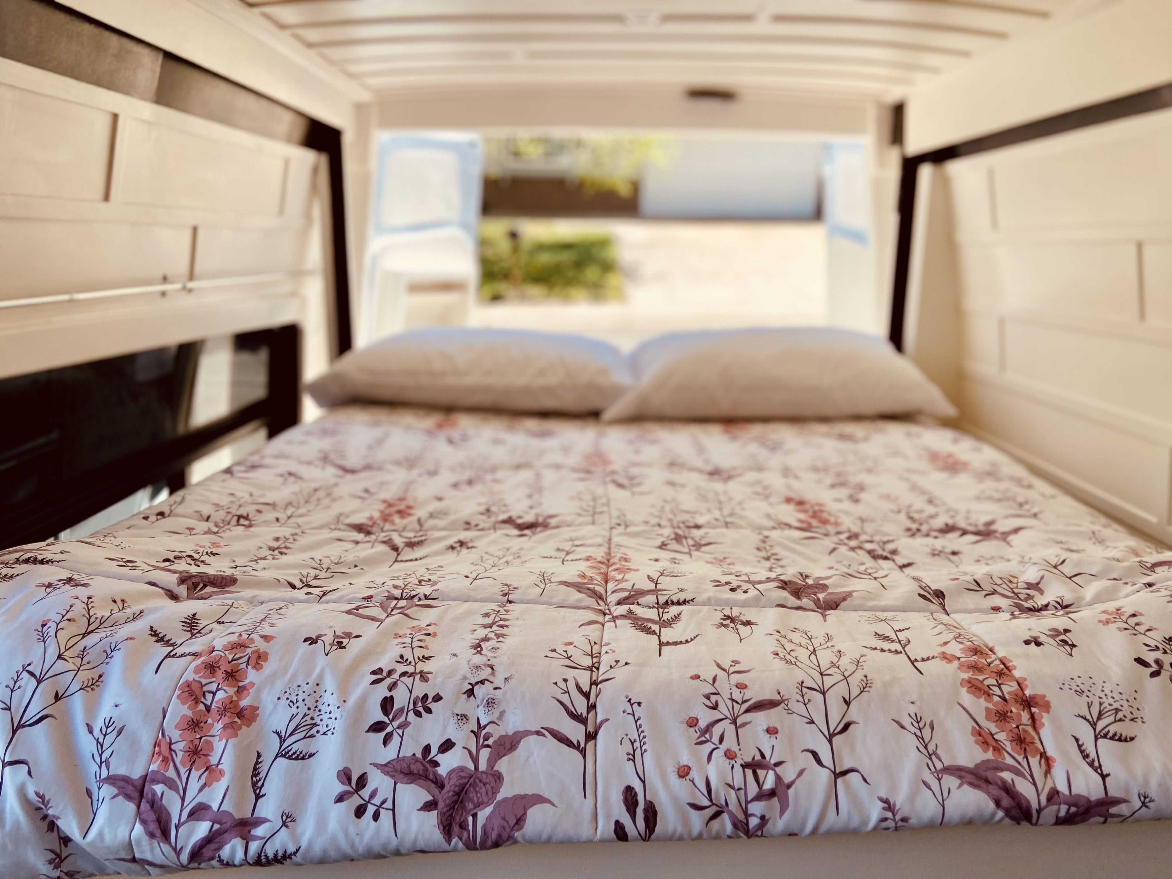 Cozy RV rental bed with a white floral comforter and pillows, showing a comfortable interior space.. Mercedes Sprinter 2021